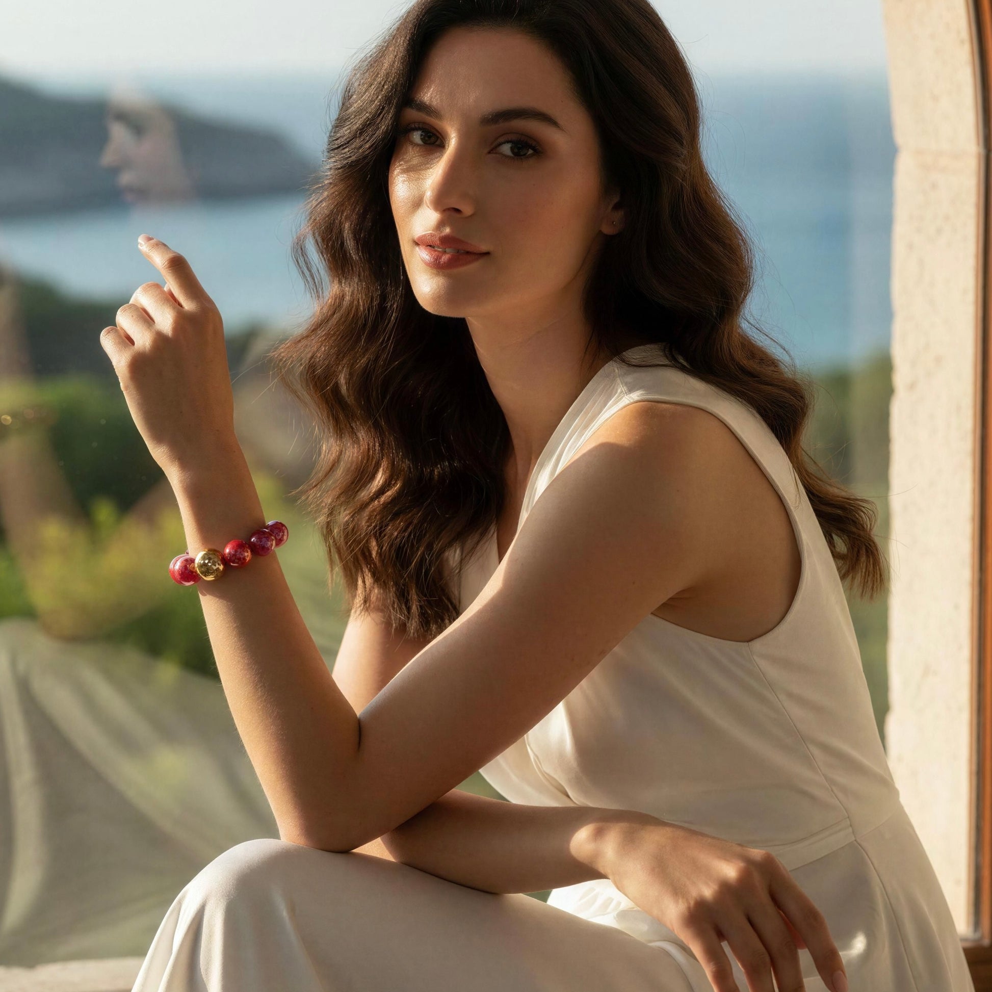 Woman in a white dress sitting outdoors with a scenic background wearing the Cherry Glow Bracelet