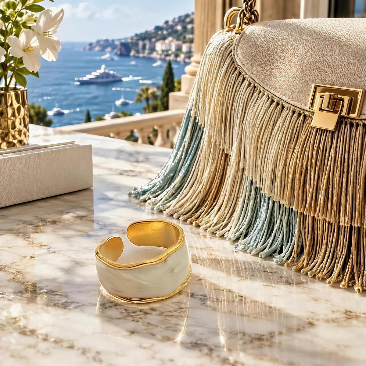 The Chica Chica Jewelry- Duna Ring - Alabastro against a marble table and silk luxurious clutch with Mediterranean hotel view.