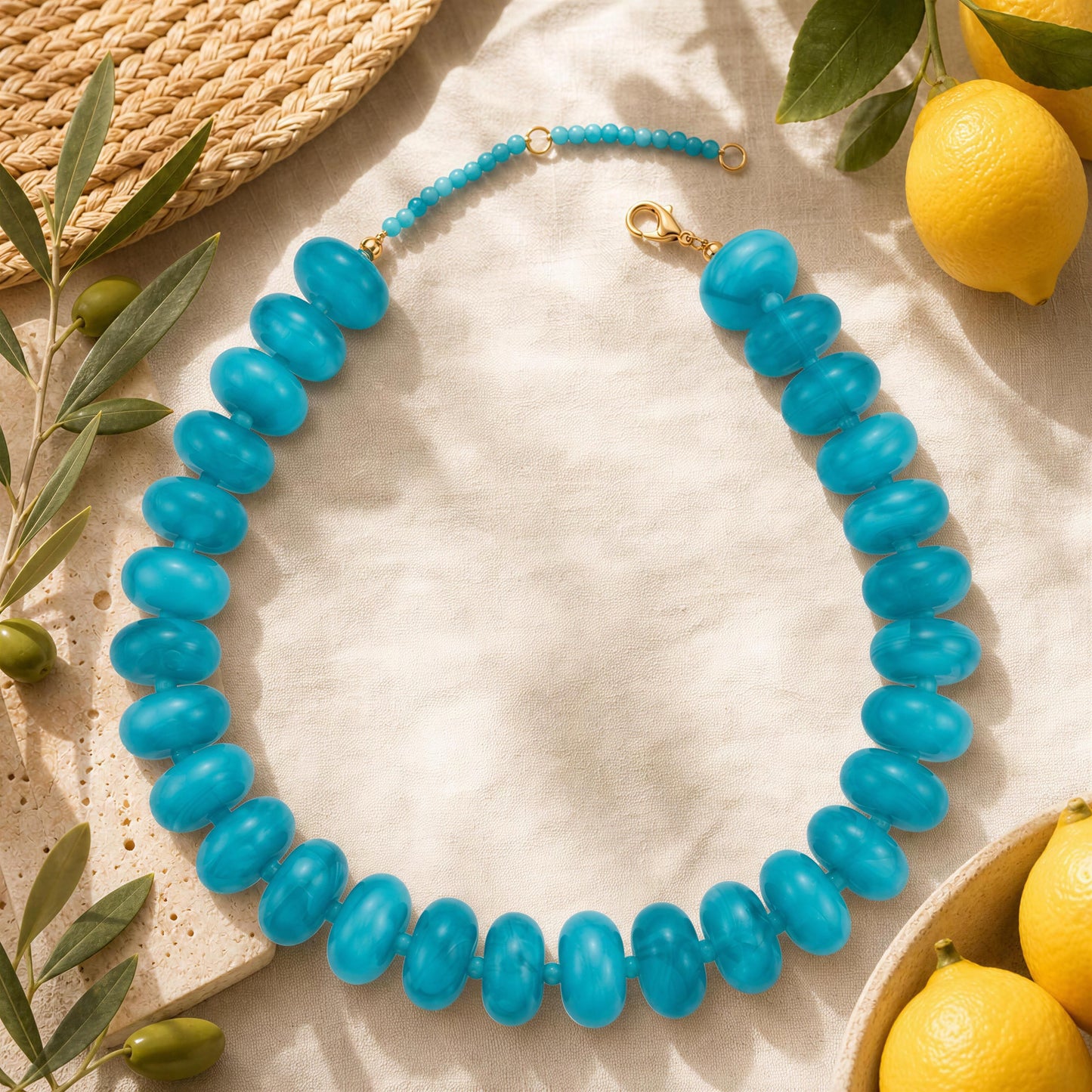 Blue 20mm resin beaded necklace on a textured surface with lemons and leaves