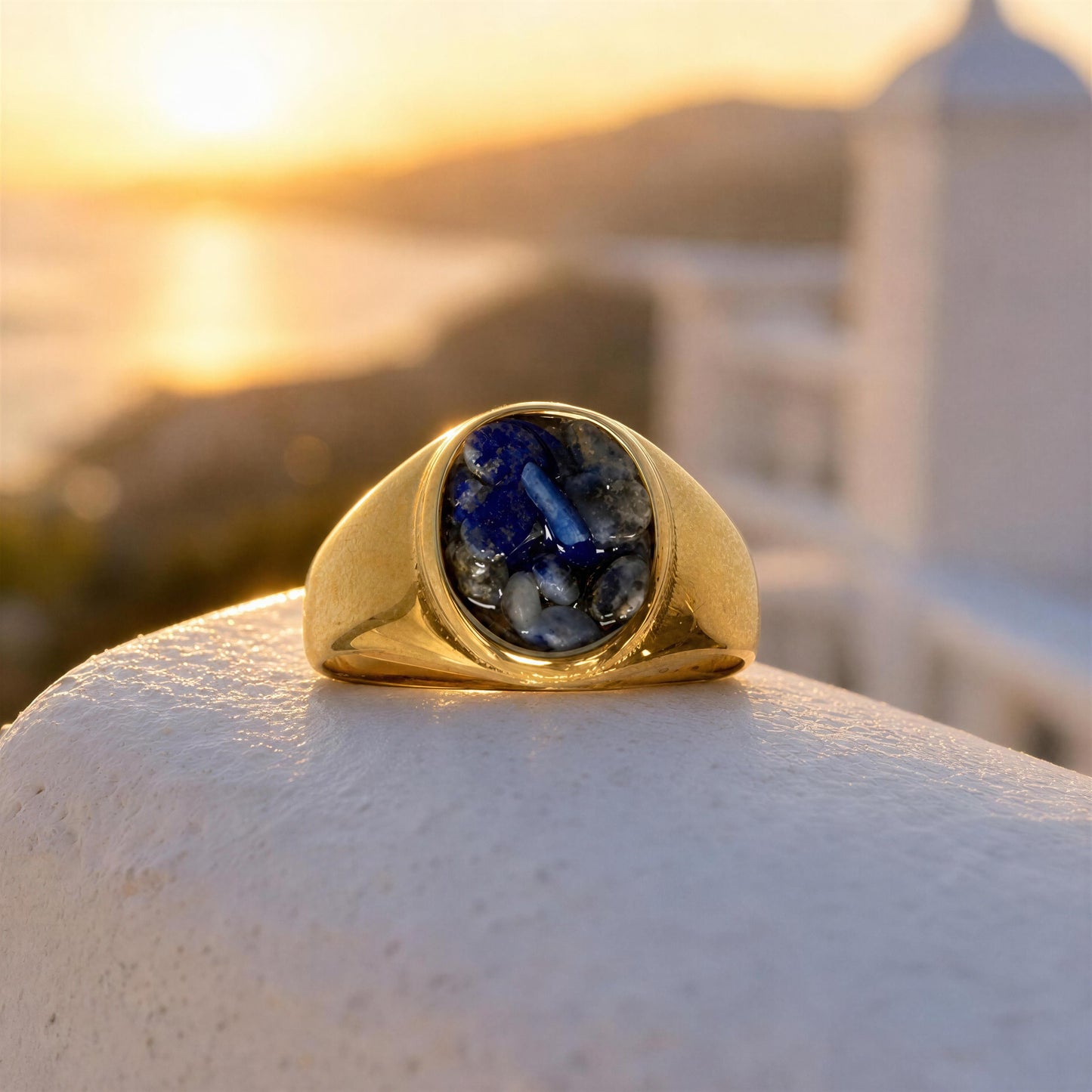 The Cosmic Blue Natural Stone Ring, resting on a white stone wall with a blurred sunset coastal background.