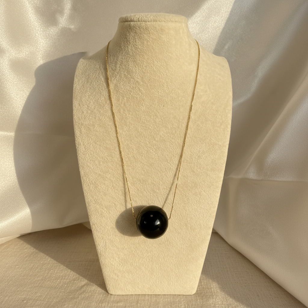 Necklace with a black pendant on a beige stand against a neutral background