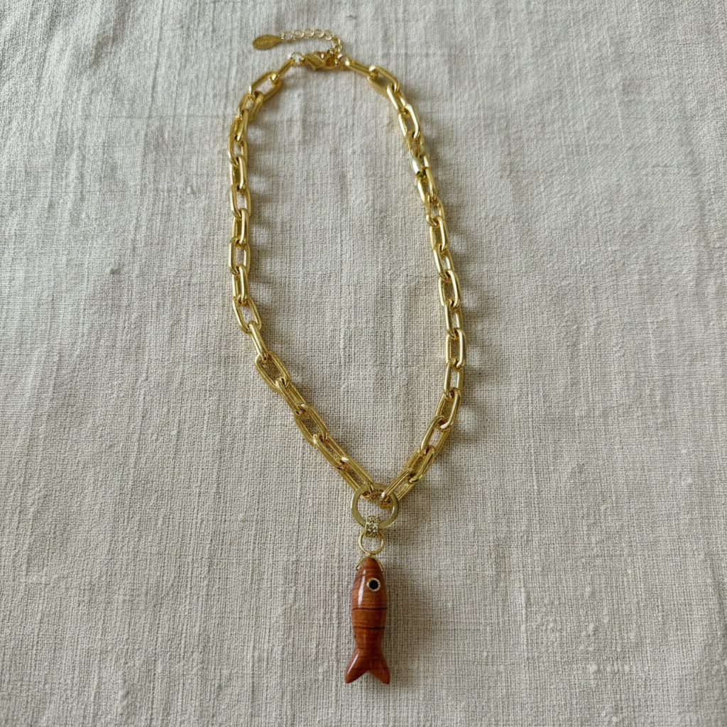 Gold chain necklace with a fish-shaped pendant on a textured beige surface