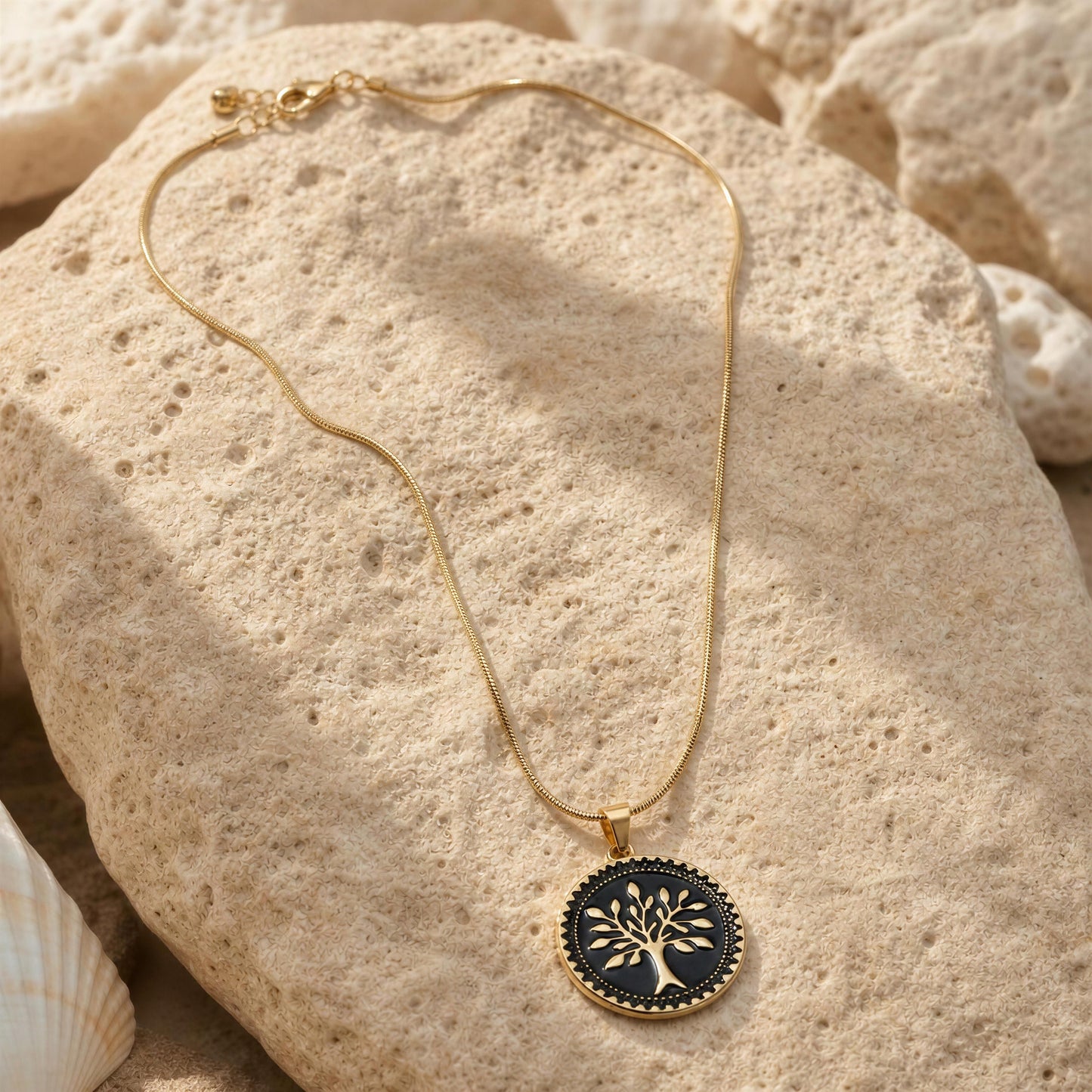 Gold necklace with a black tree pendant on beige stones