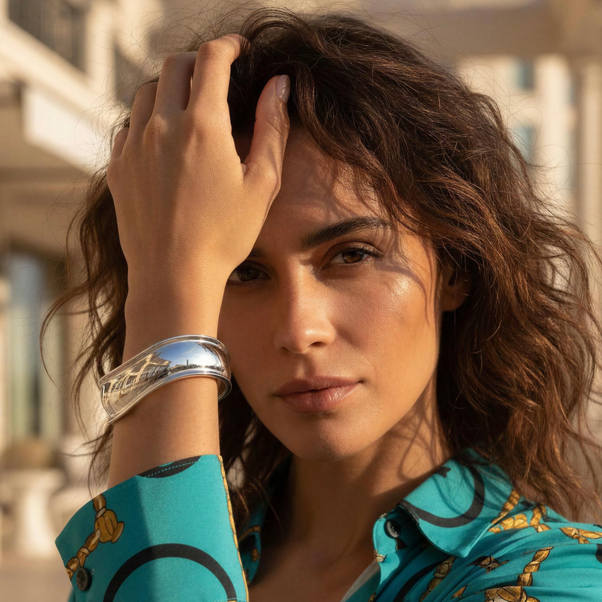 Model wearing the Forma Cuff in polished silver with a turquoise blouse featuring gold chain prints, highlighting its bold sculptural curves and reflective finish.
