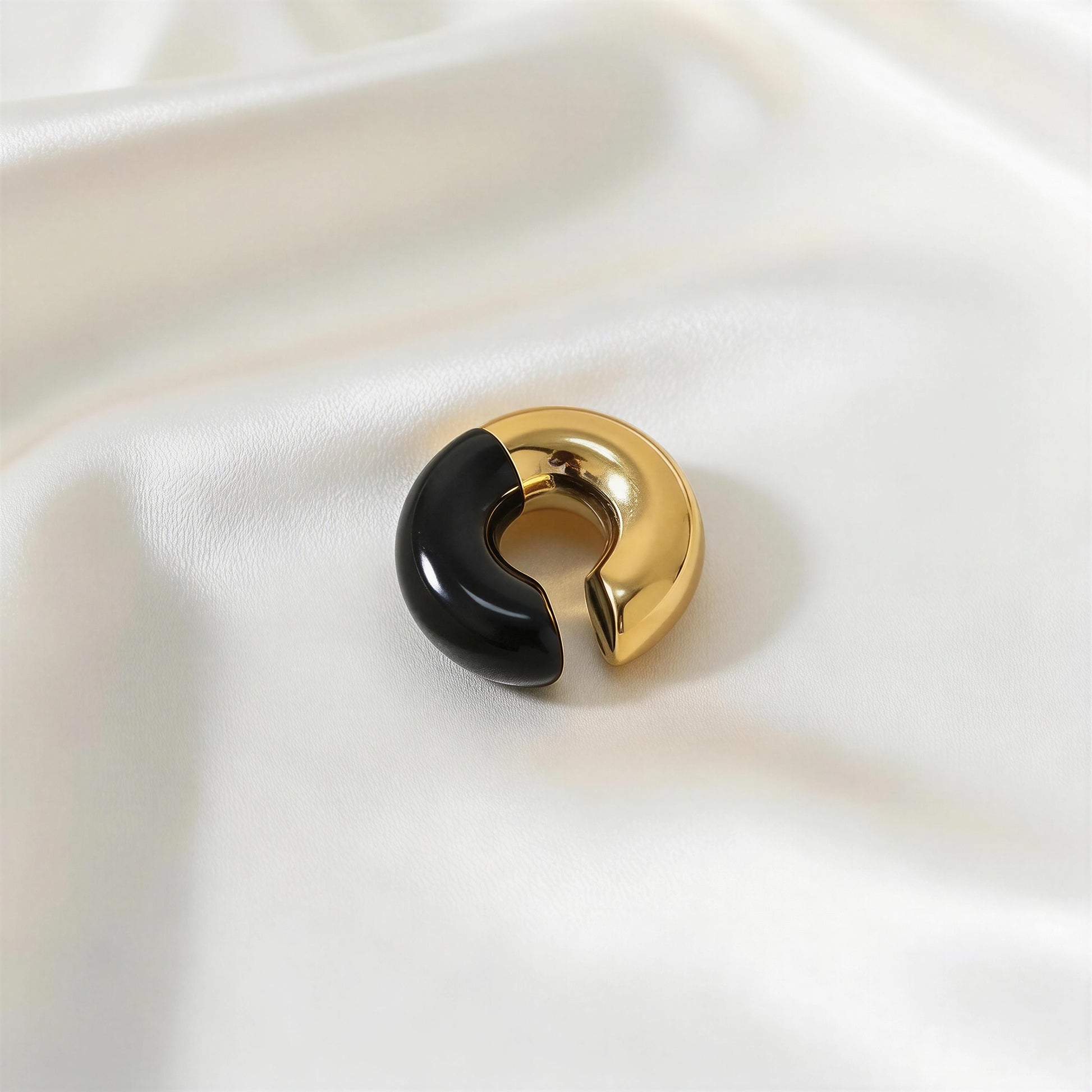 Gold and black ear cuff on a white fabric background