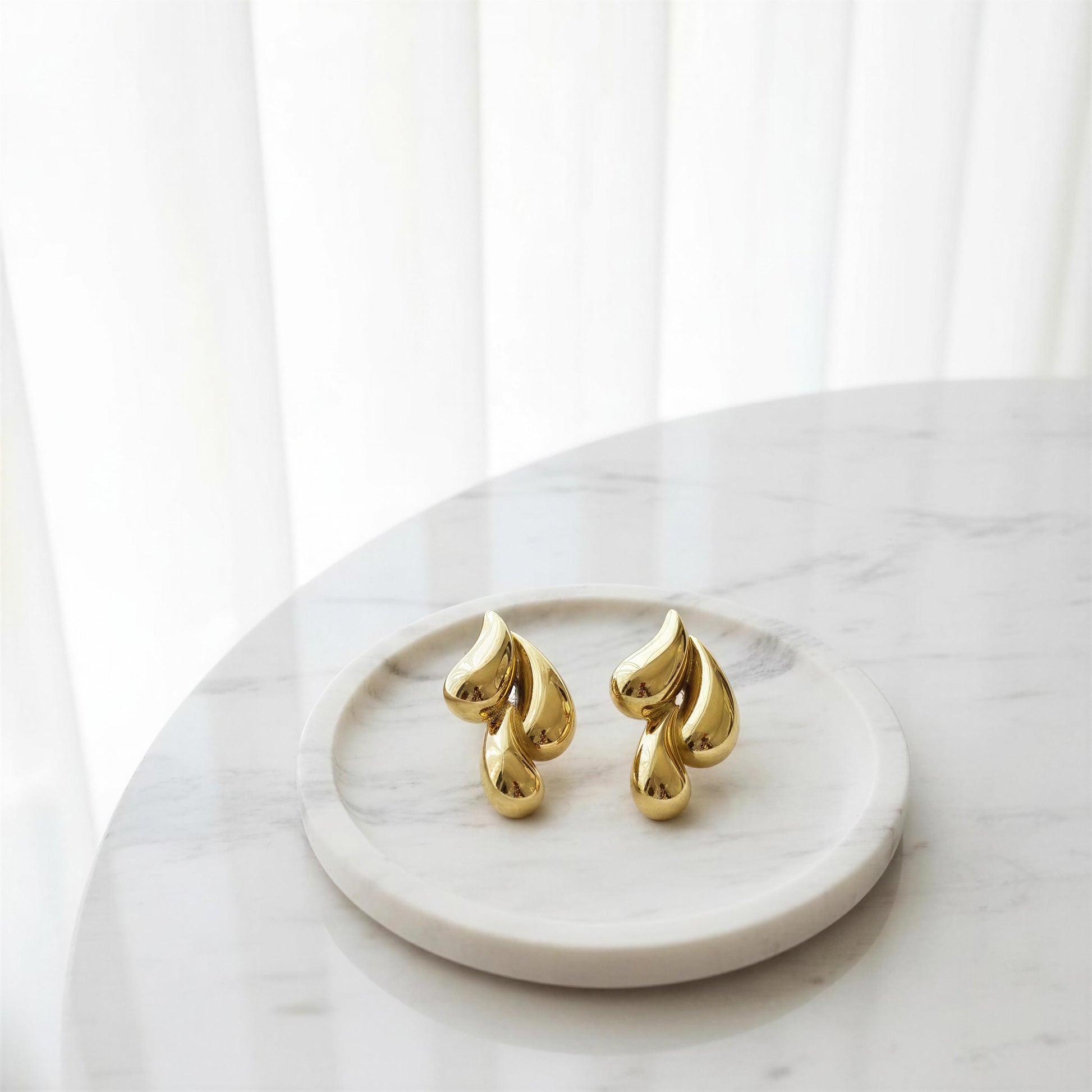 The Golden Molten Wave Drops on a marble surface with a white curtain background