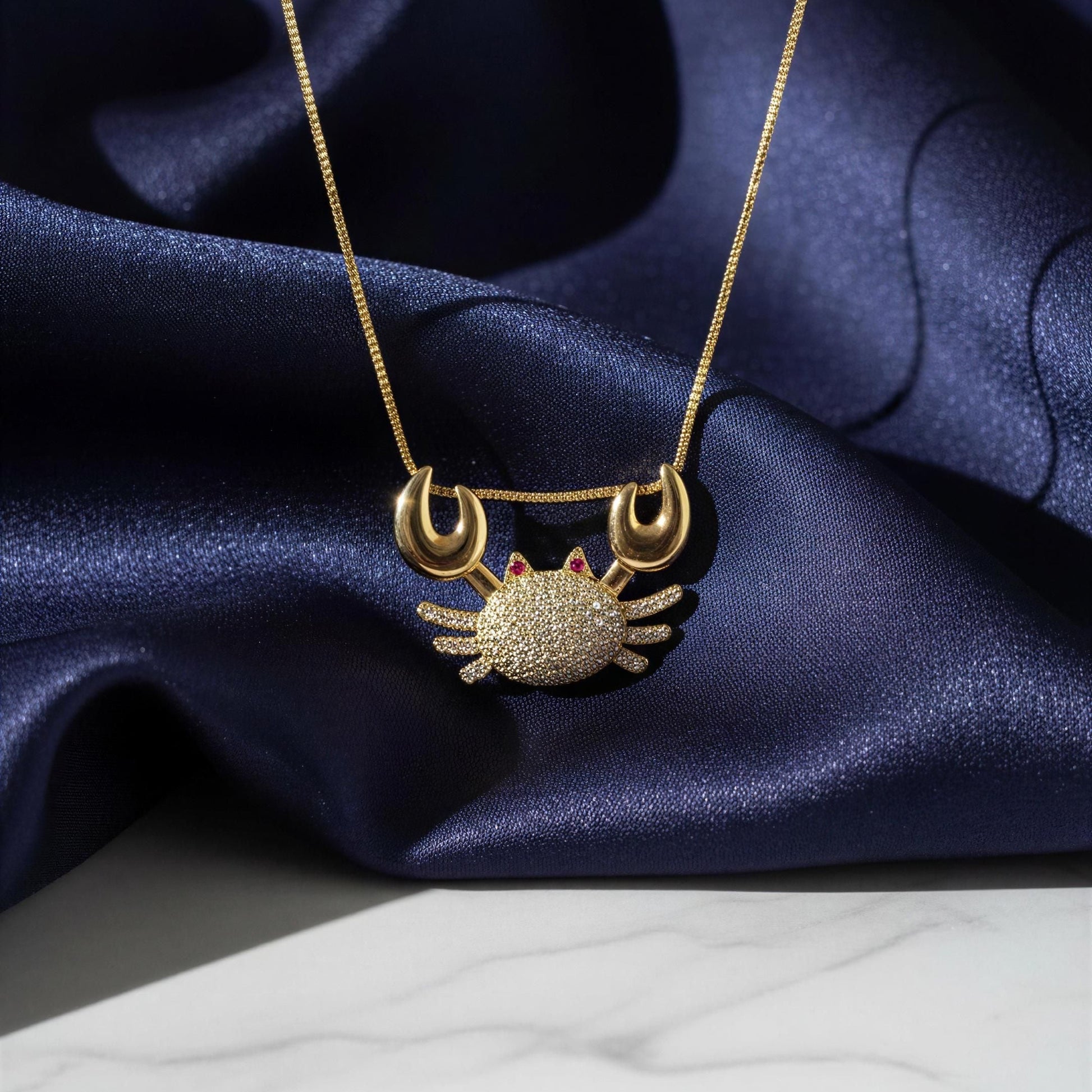 Gold crab-shaped pendant necklace on a blue satin fabric background