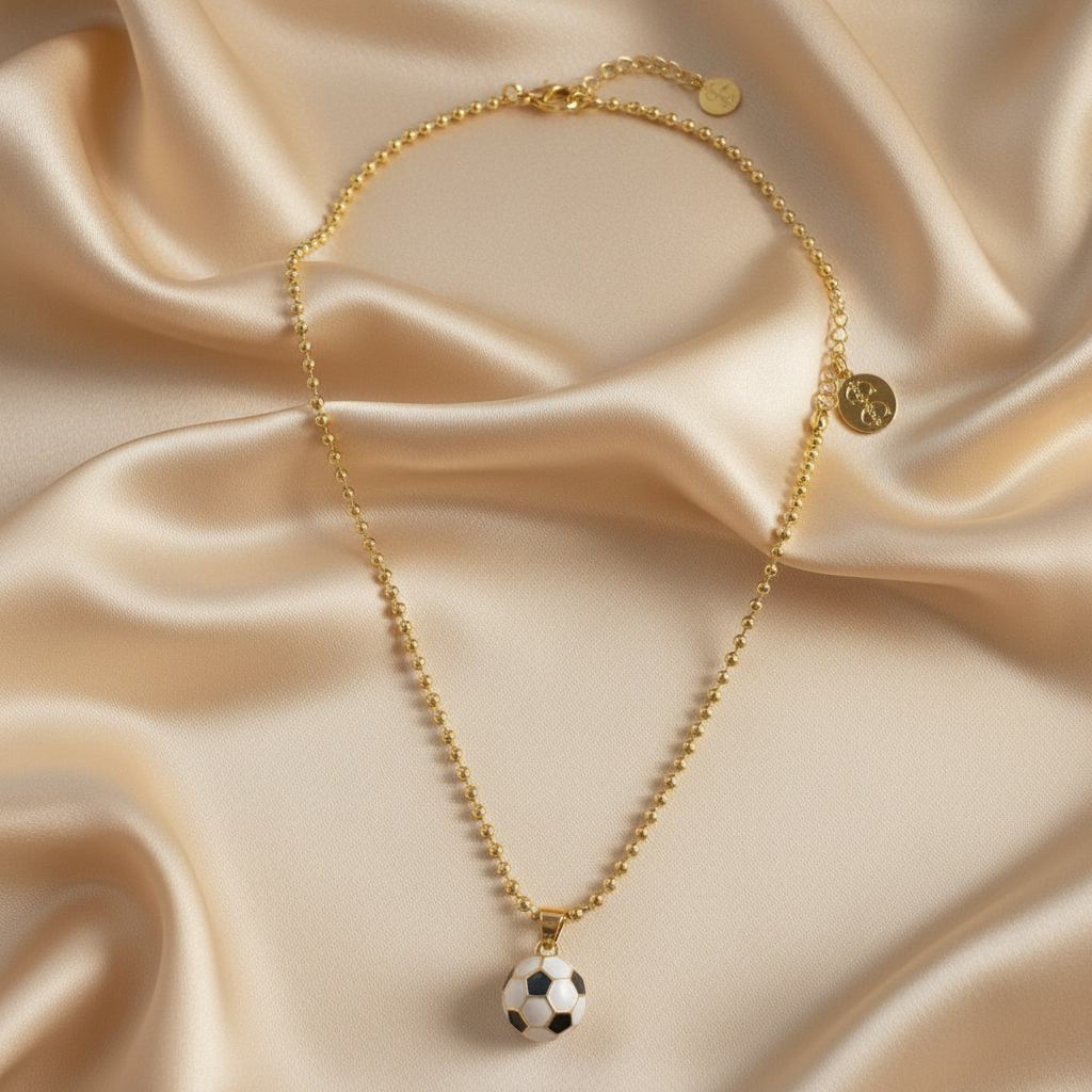 Gold soccer ball charm necklace displayed on champagne-colored silk fabric highlighting enamel detail and gold finish