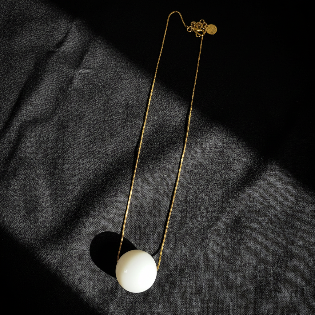 The Milky Bead Necklace with a white pendant on a black fabric background