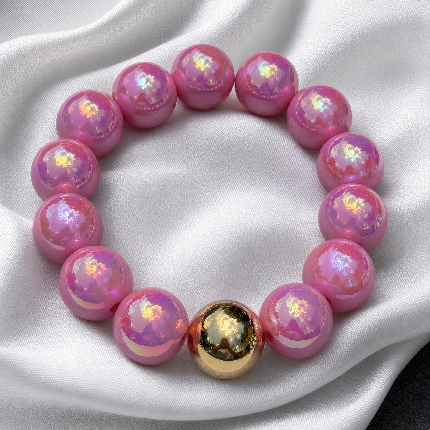 Pink beaded bracelet with a gold accent on a white fabric background