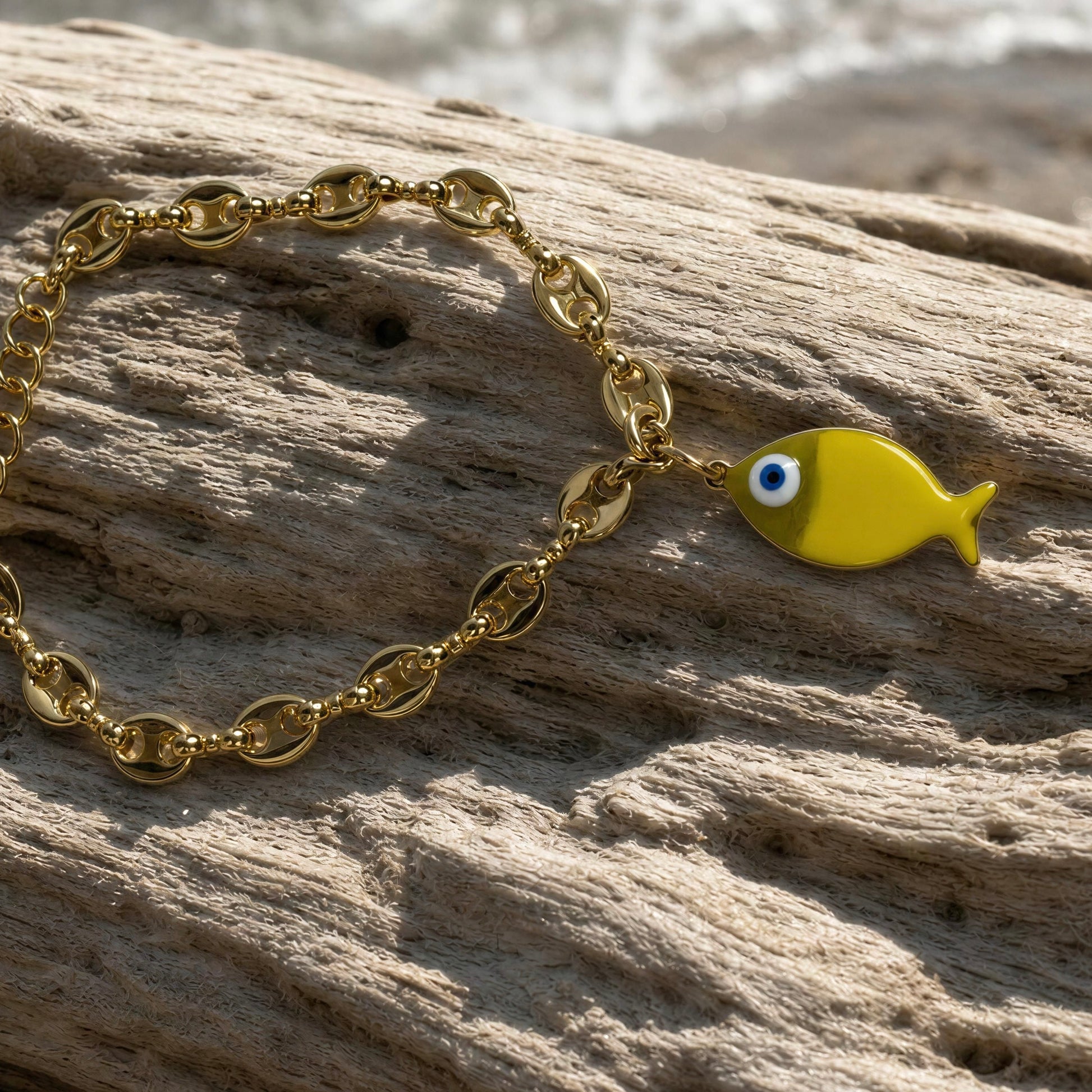 Gold bracelet with a yellow fish charm on a wooden surface