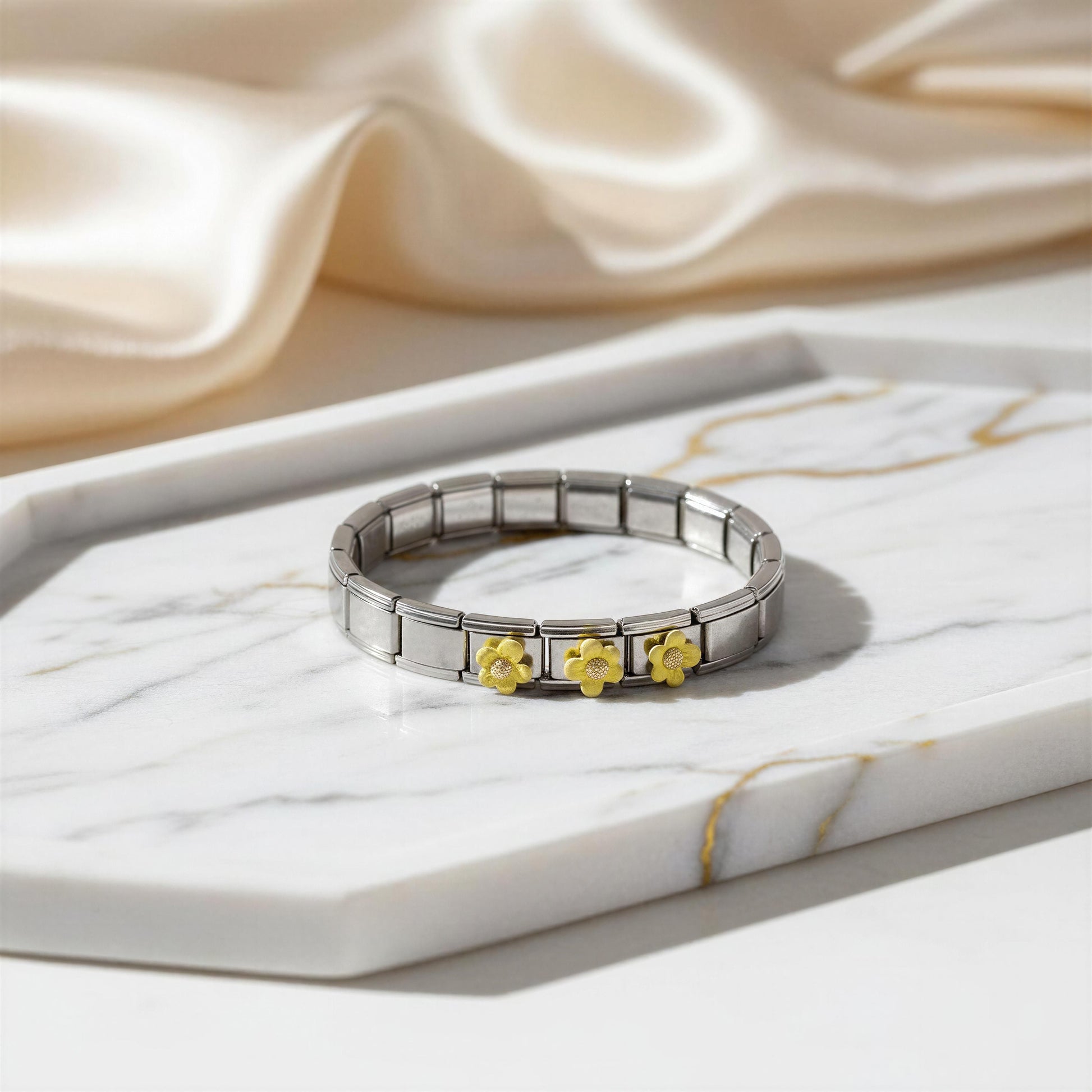Silver bracelet with gold flower charms on a marble surface