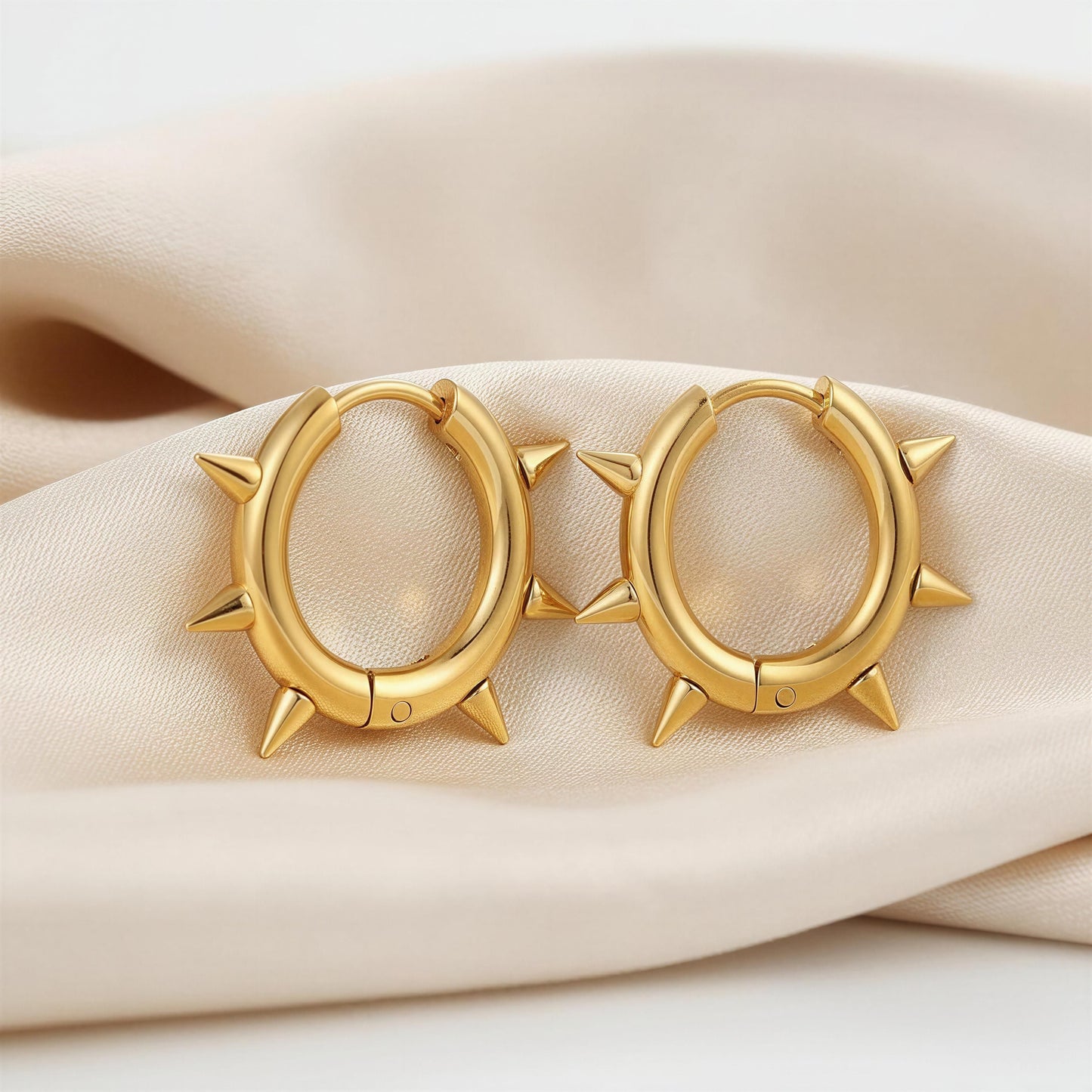 Gold hoop earrings with spike details on a beige fabric background