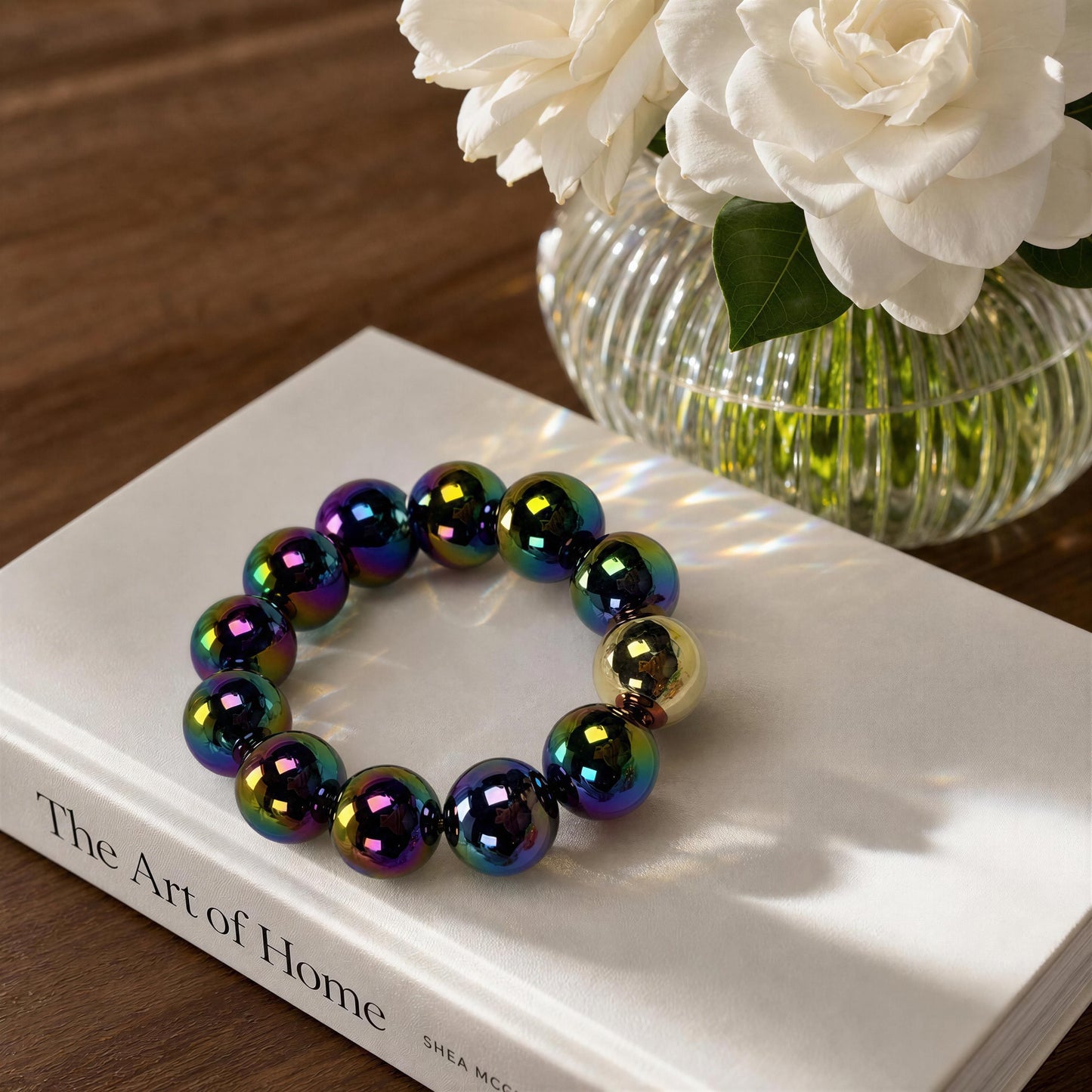 The Velvet Plum Bracelet on a book with a vase of white flowers in the background