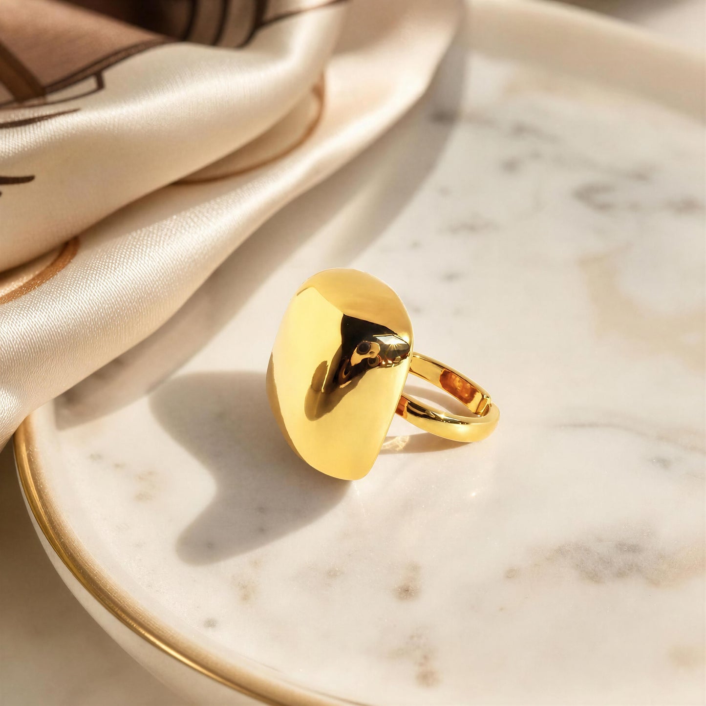 A polished gold square, resting on a white marble plate with gold trim next to a cream satin fabric.