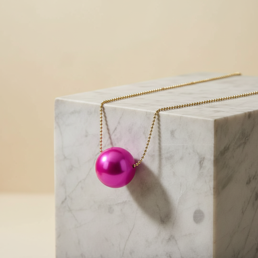 The Carmín Petite Sphere Necklace on a marble surface