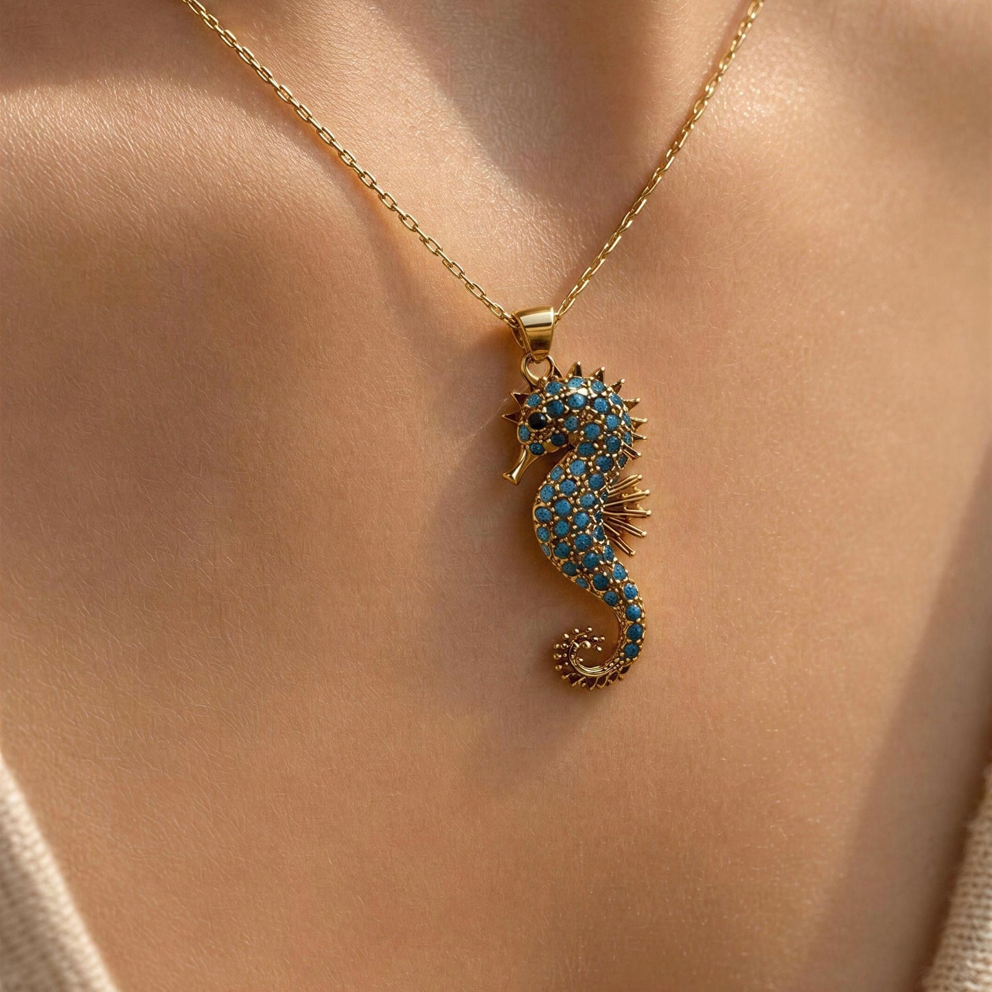 A gold seahorse pendant necklace embellished with blue and clear rhinestones, worn on a model's neck.