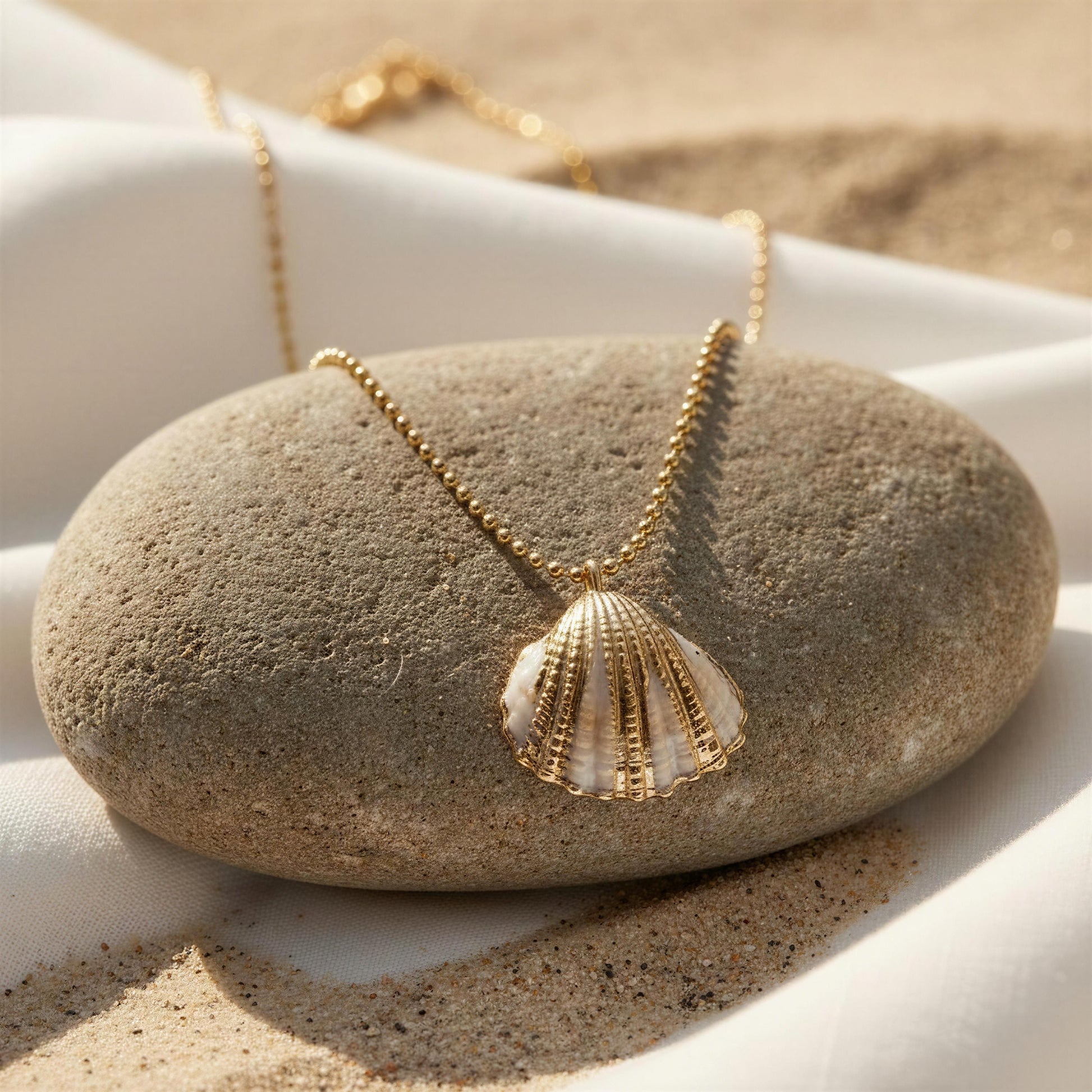 Gold necklace with a shell pendant on a stone surface