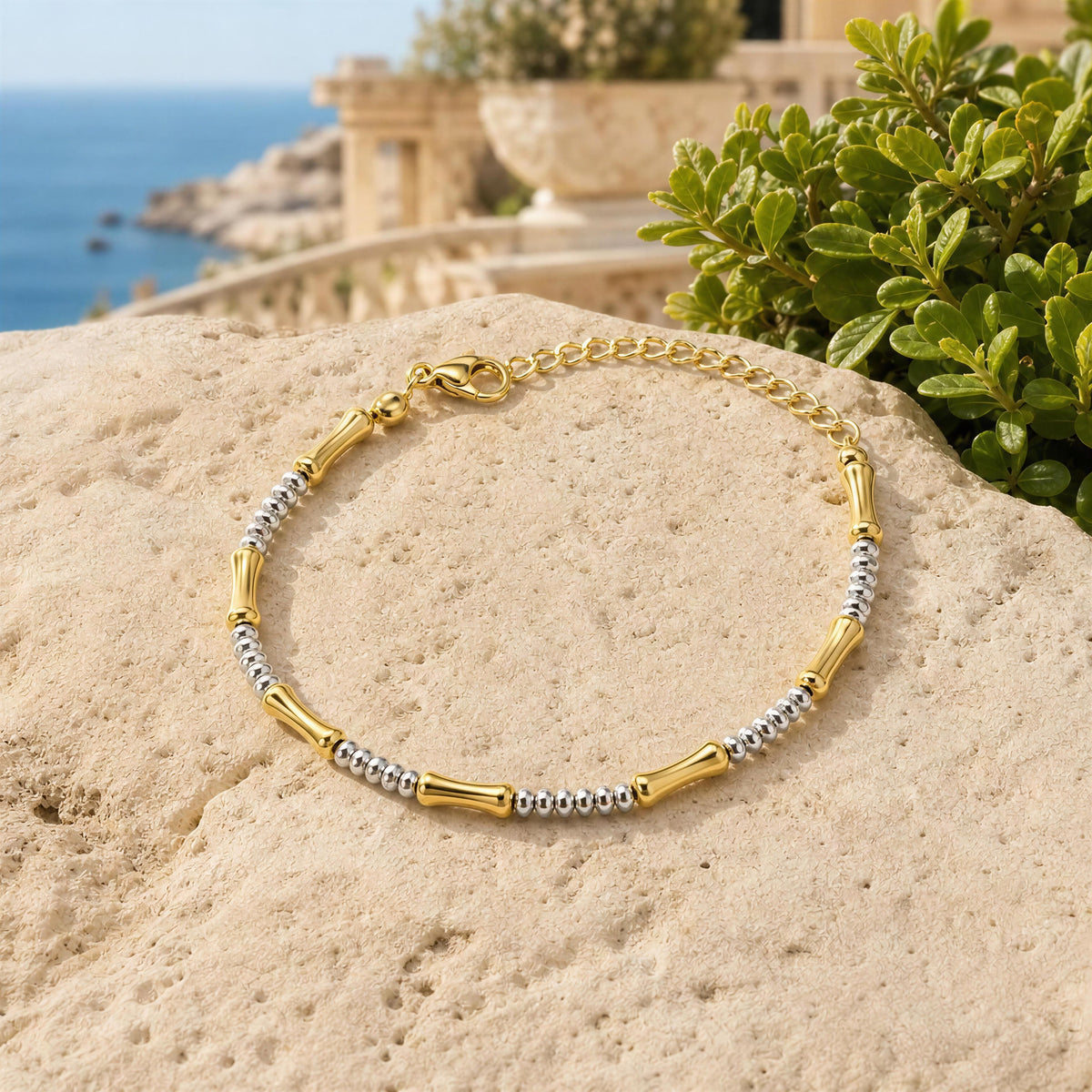 The Chica Chica Jewelry Malta Bracelet , displayed on a beige stone with a coastal background featuring green foliage and the sea.