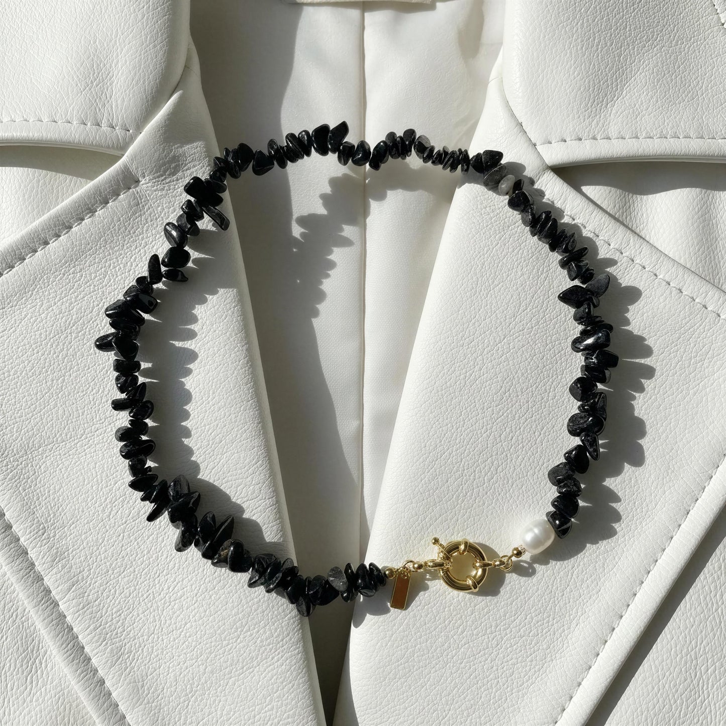 The Midnight Tide Necklace with a gold clasp on a white textured surface