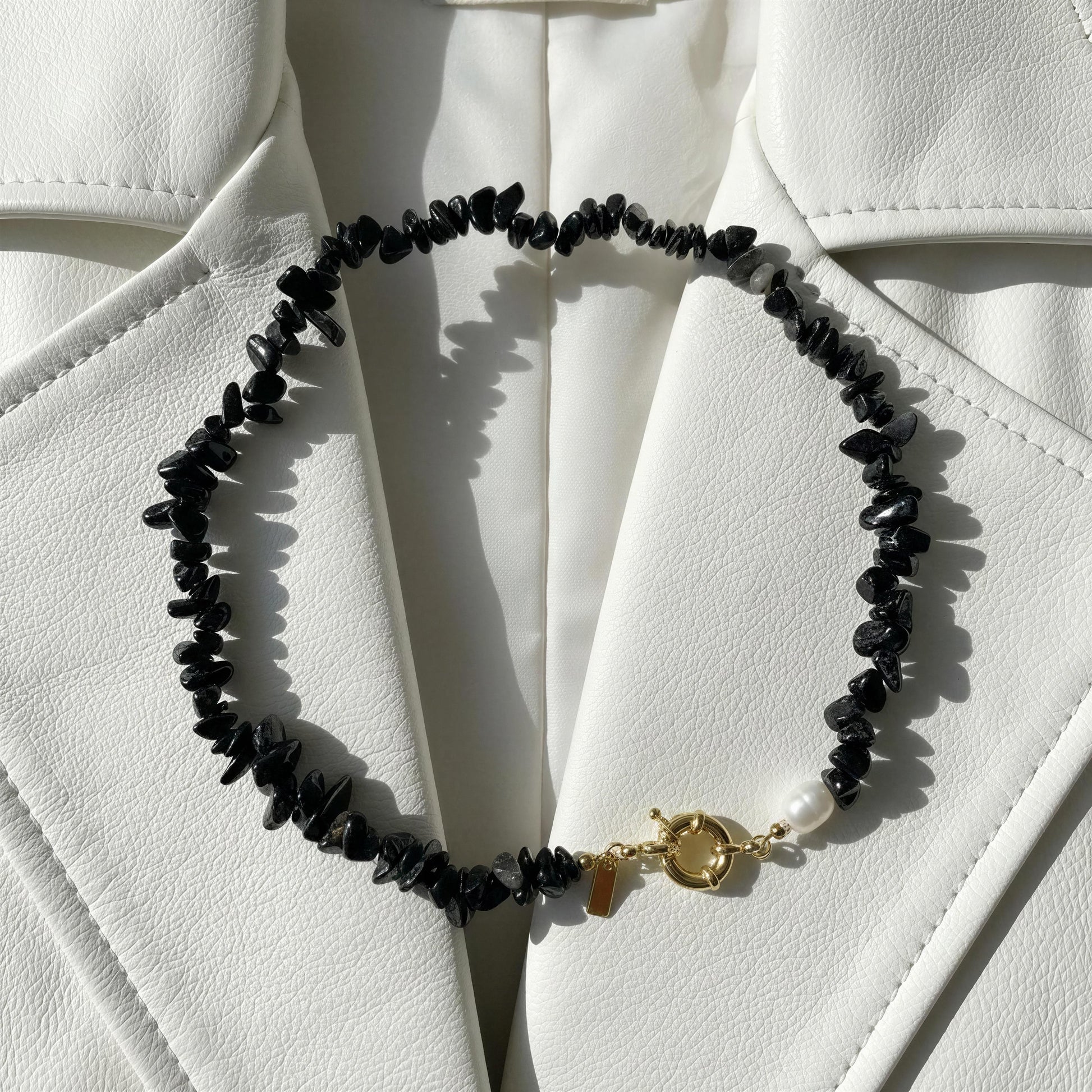 The Midnight Tide Necklace with a gold clasp on a white textured surface