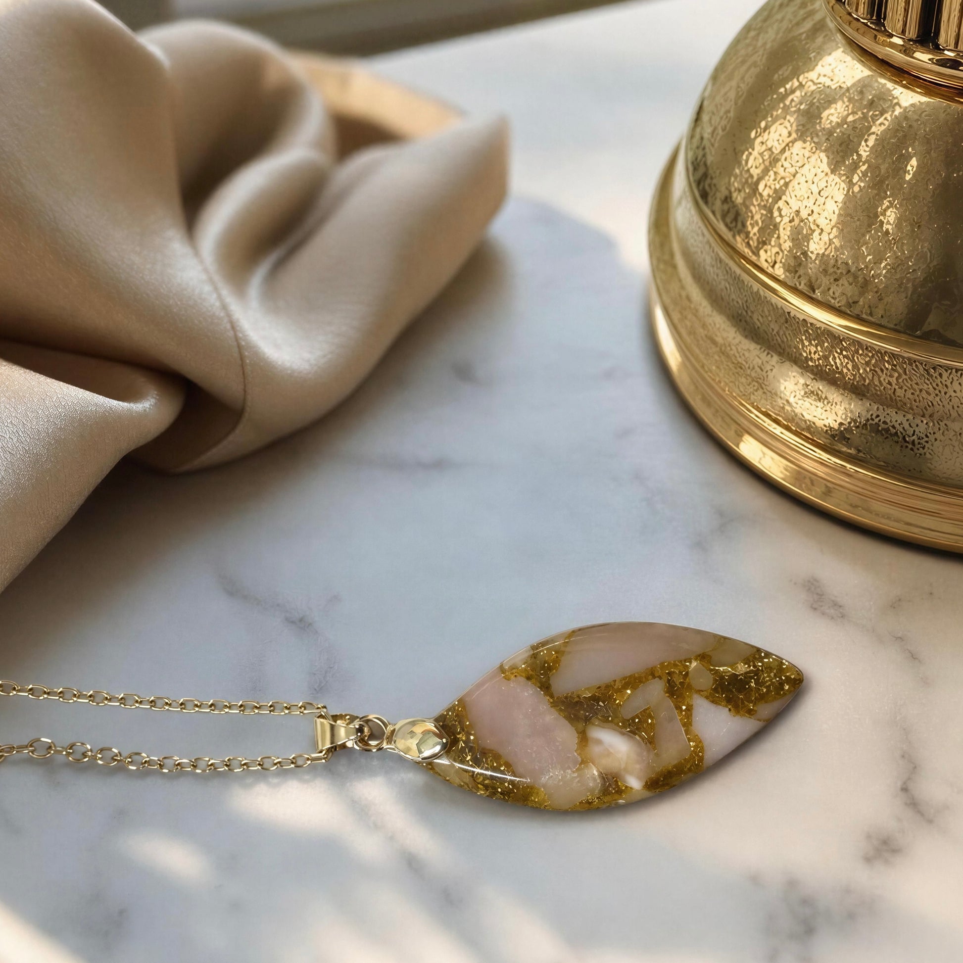 The Pietra Cipria Natural Stone Necklace, displayed on a white marble surface next to a beige fabric and a gold bell.