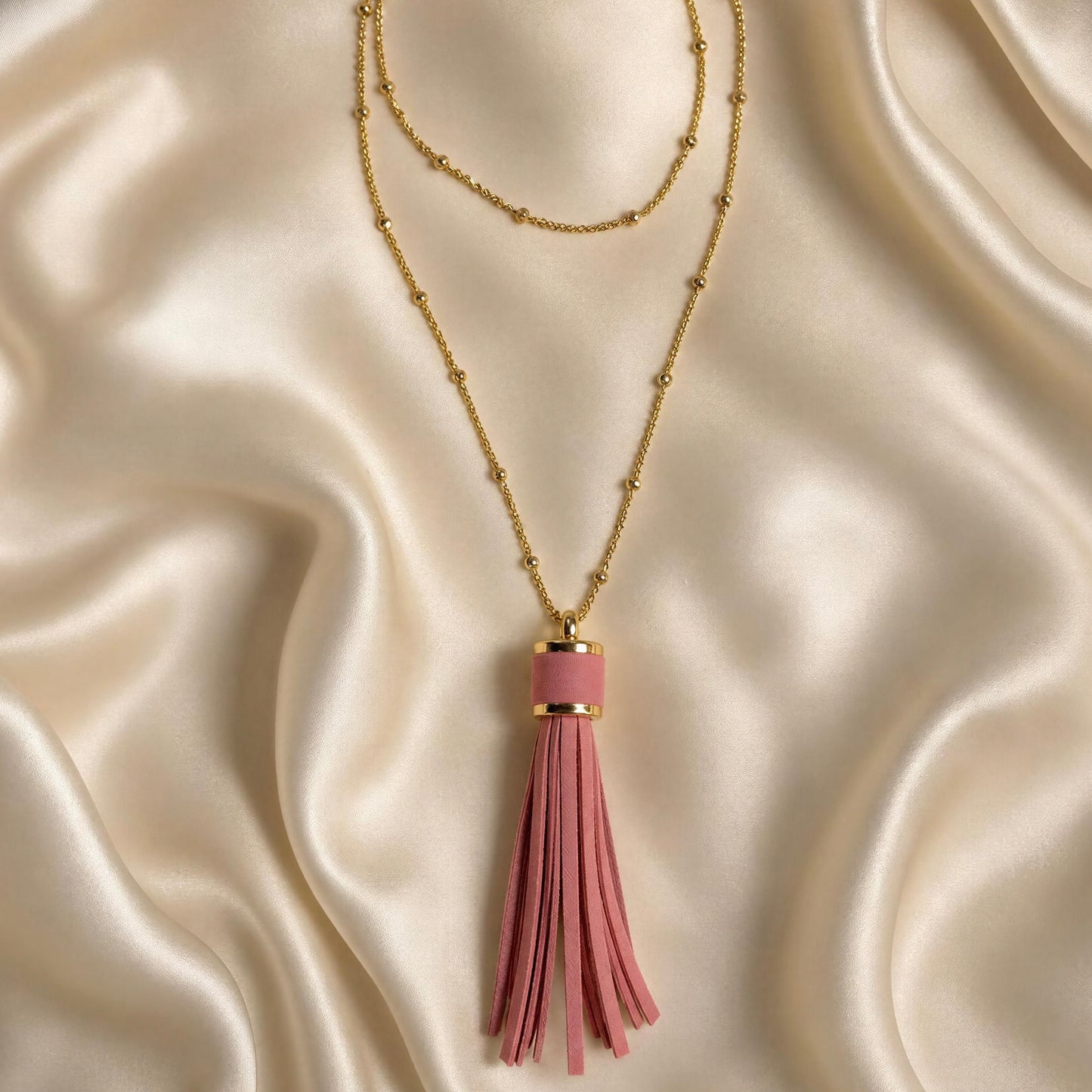 A gold layered necklace featuring the Frangia Rosa Necklace from Chica Chica Jewelry,  displayed on a draped cream satin fabric background.