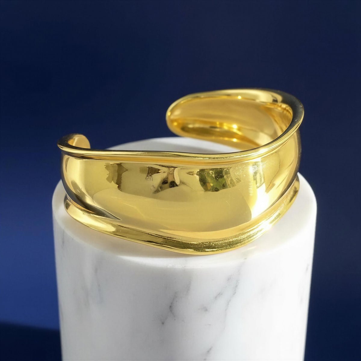 Close-up of Forma Gold sculptural cuff bracelet on white marble pedestal