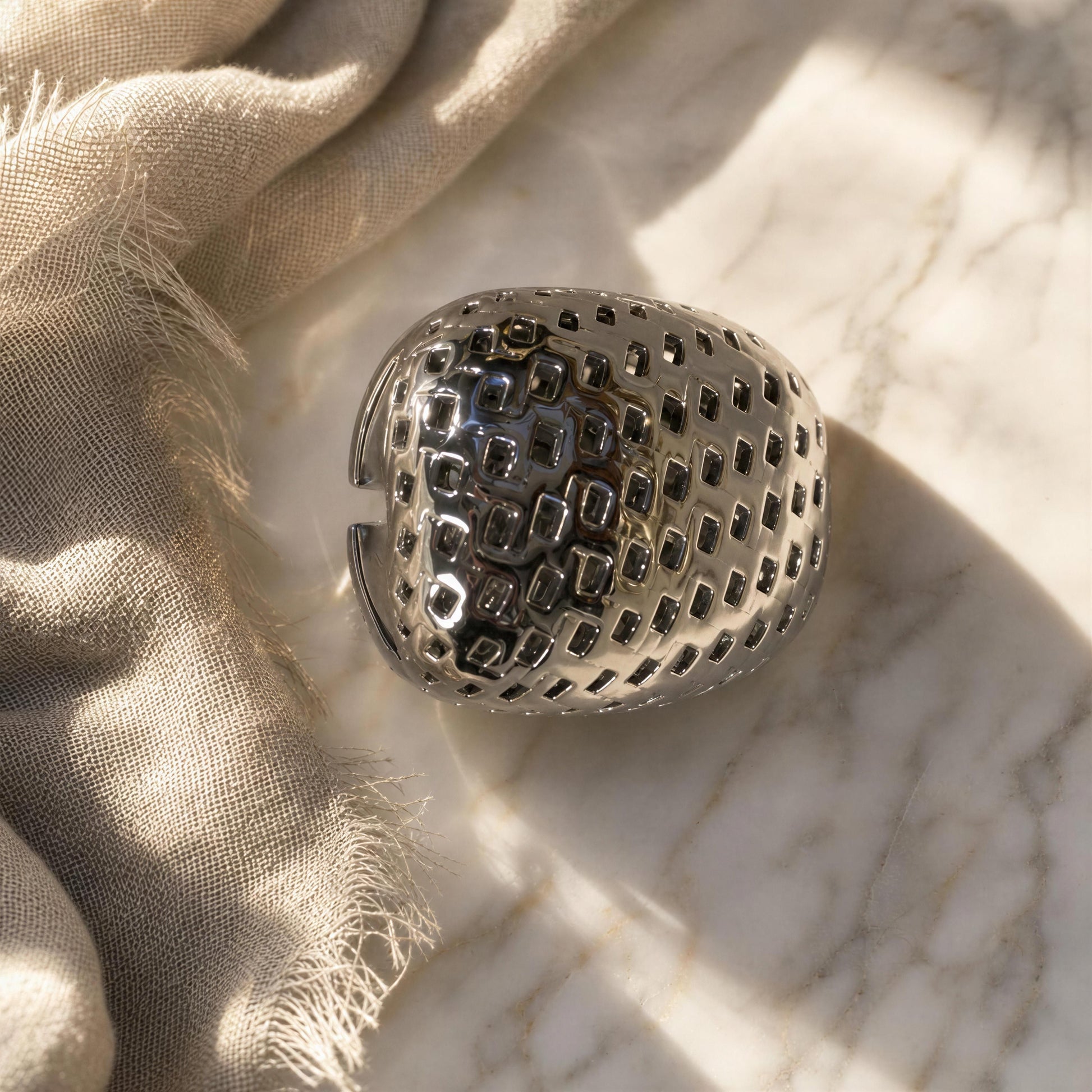 The Trama Ring Silver, styled on a marble surface next to a beige linen cloth.