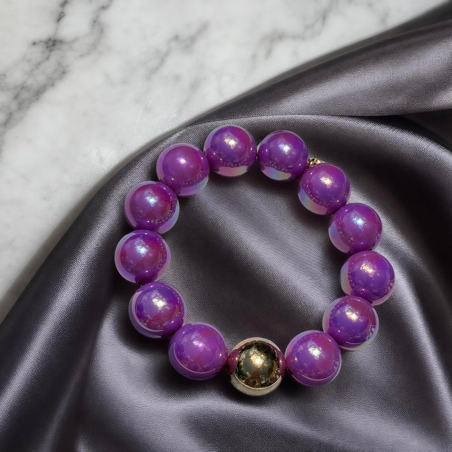 Purple beaded bracelet on a gray fabric surface with a marble background