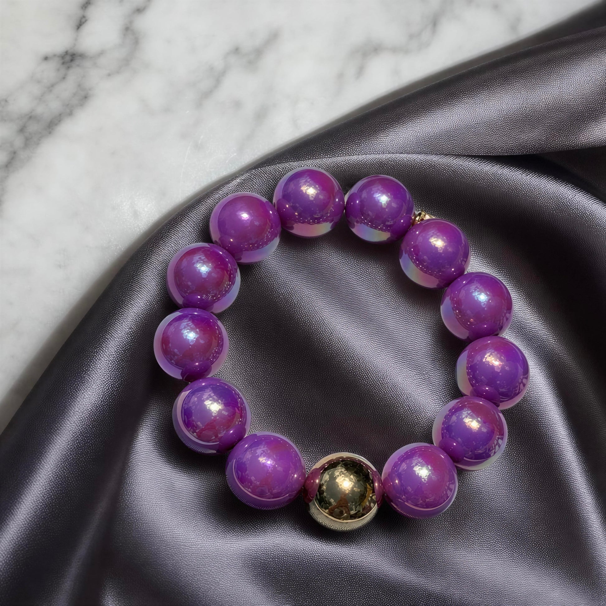 Purple beaded bracelet on a gray fabric surface with a marble background