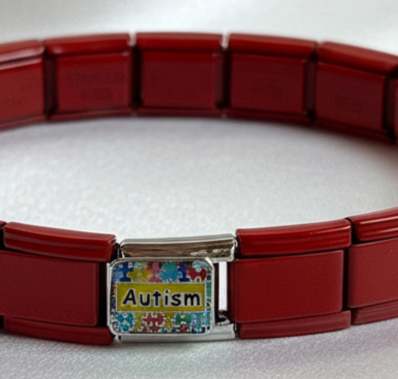 Close-up of autism awareness charm on red stainless steel Italian link bracelet

