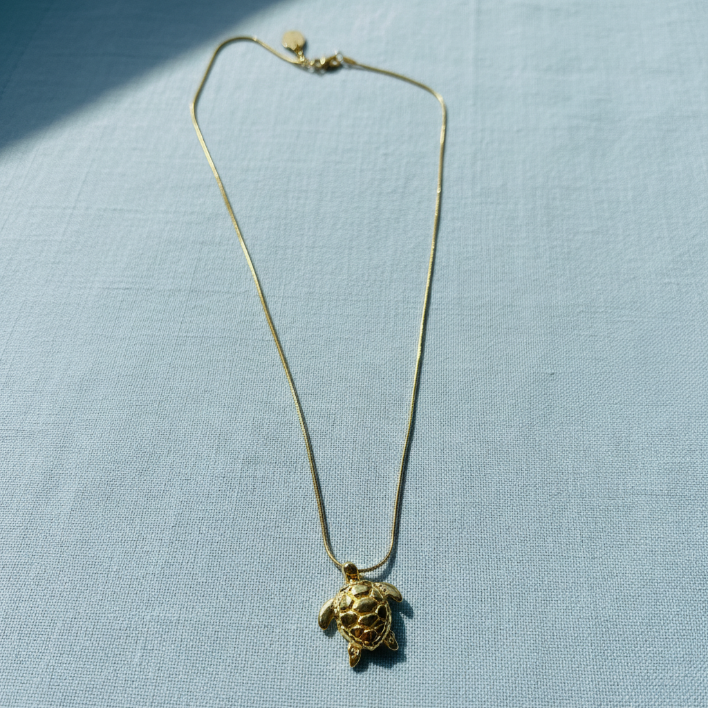 Golden Harbor Turtle Necklace on a light blue fabric background