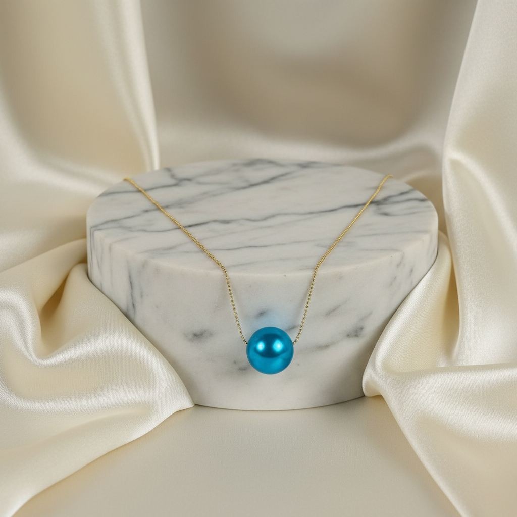 The Cielo Petite Sphere Necklace with a blue pendant on a marble stand with beige fabric background