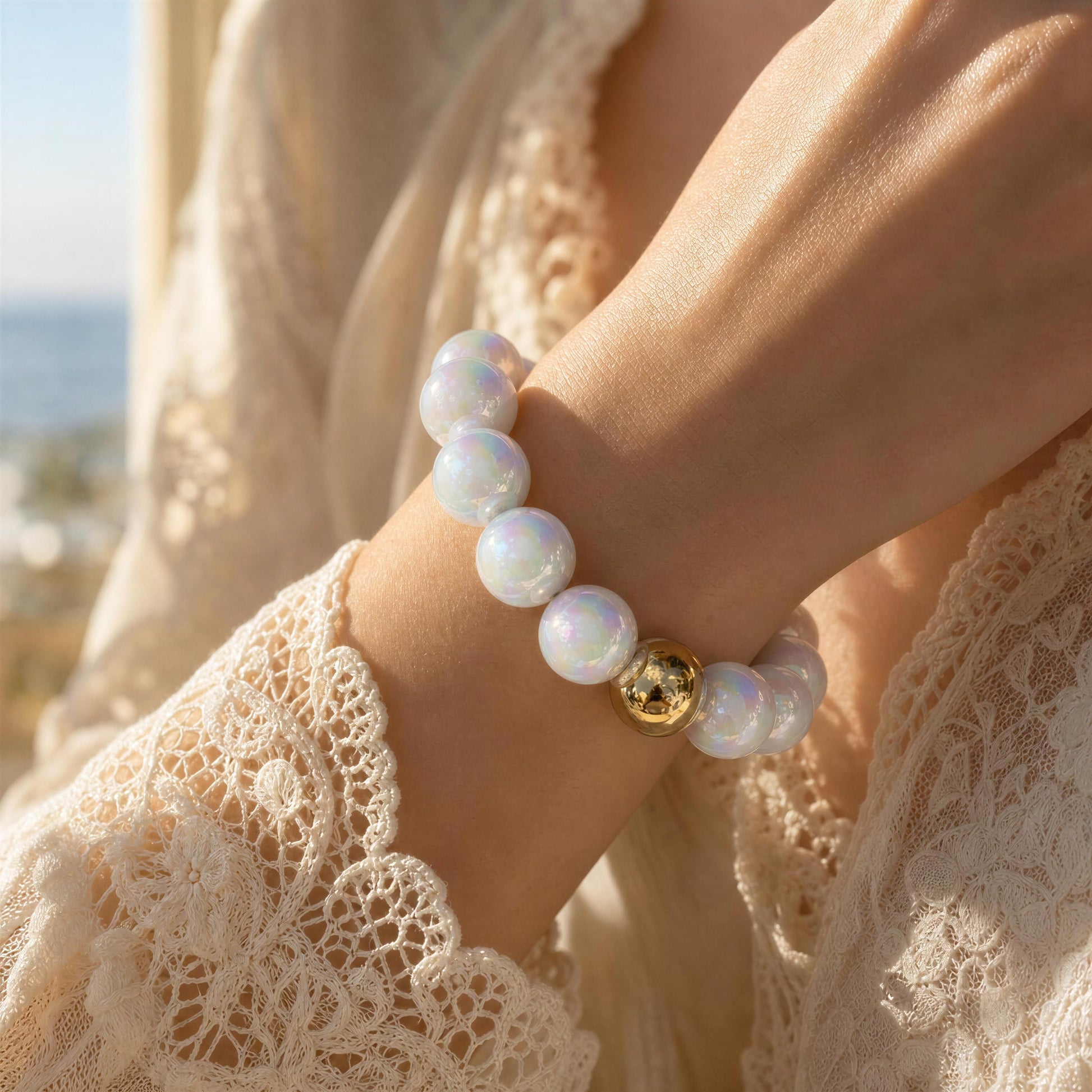 White glossy bracelet with a gold accent on a person's wrist, wearing a lace garment with a blurred outdoor background.
