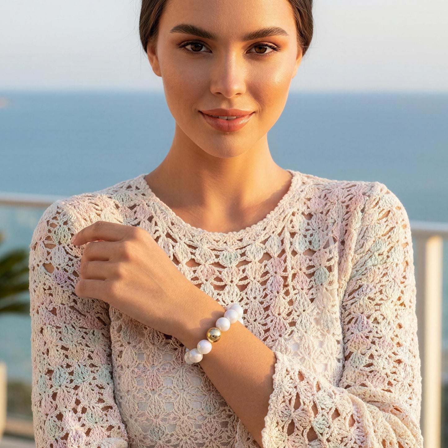 Woman wearing the Coconut Glow Bracelet and a  crochet dress with a blurred ocean view in the background