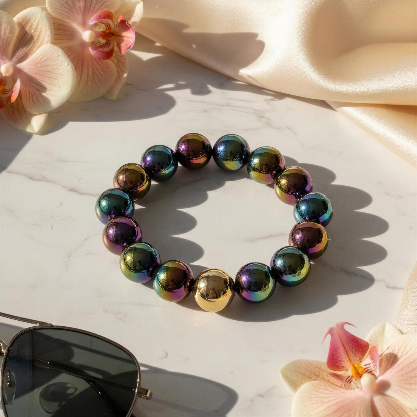 The Velvet Plum Bracelet on a light surface with pink orchids and sunglasses.