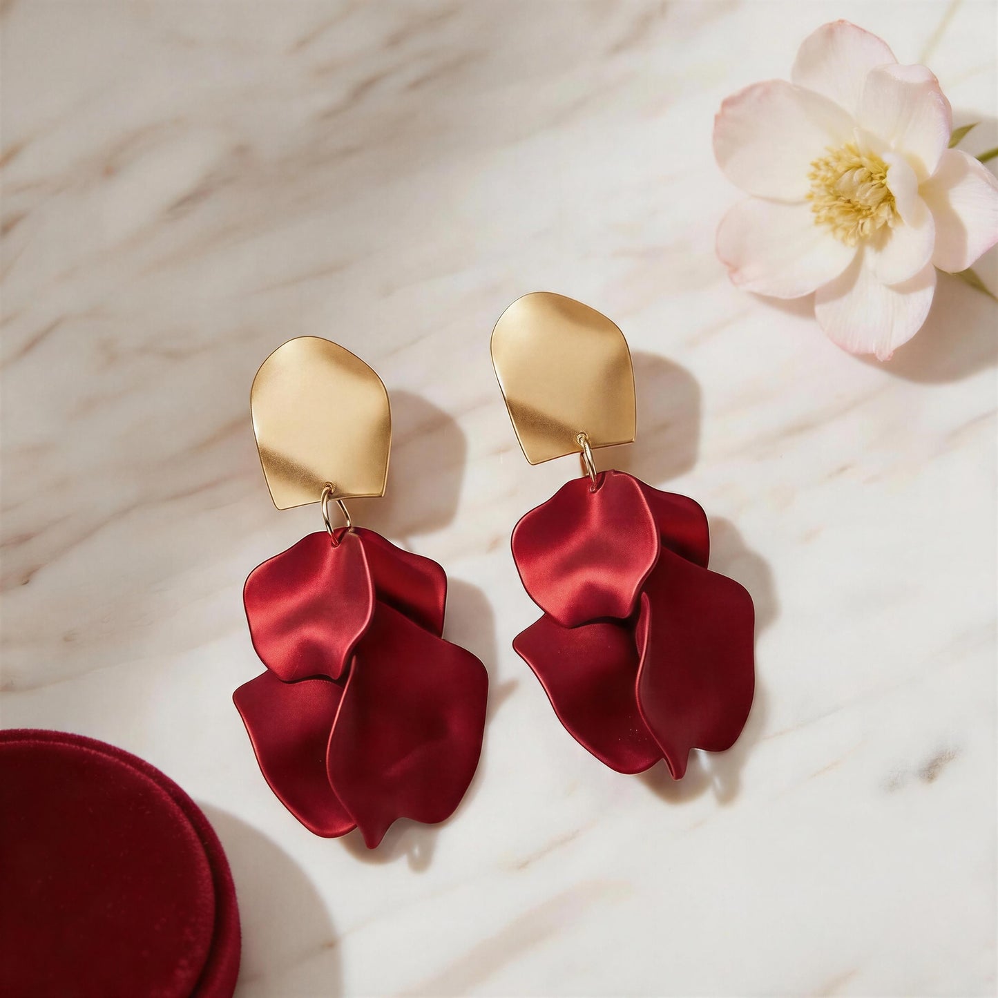 The Crimson Bloom Earrings on a marble surface with a flower.