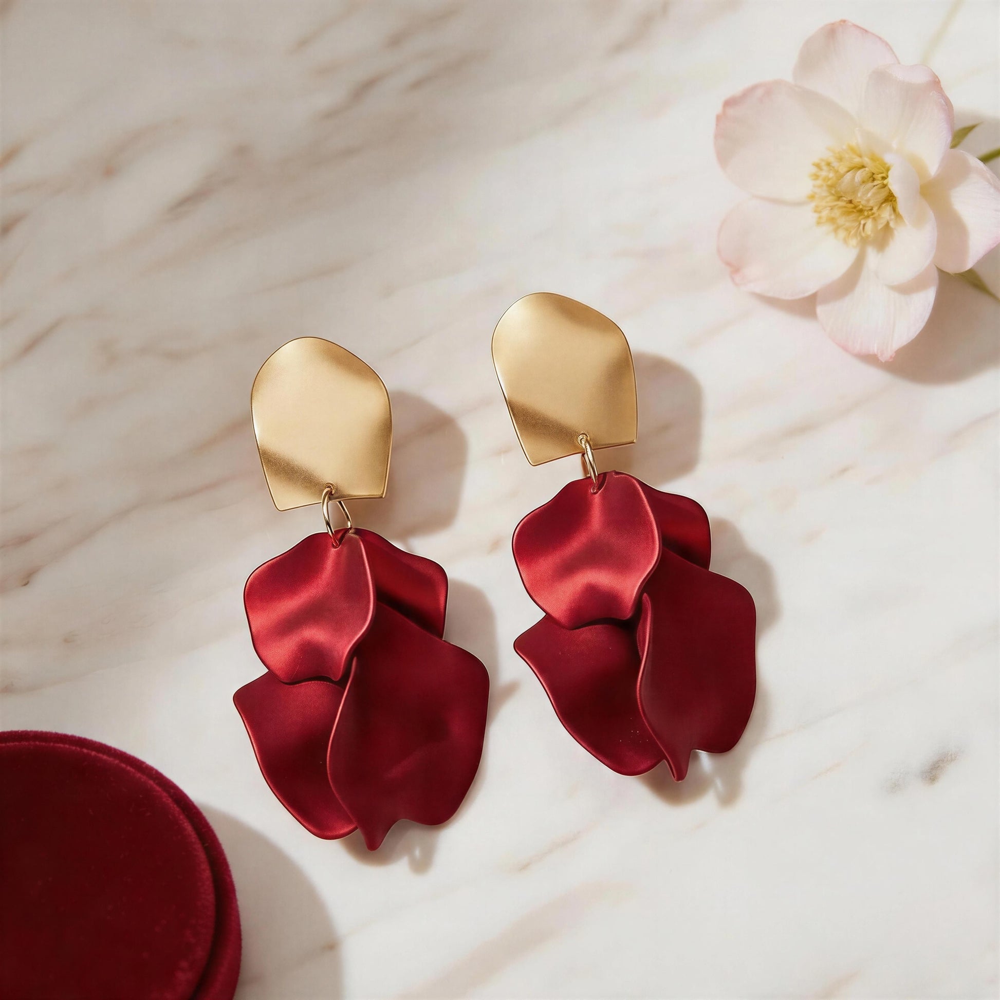 The Crimson Bloom Earrings on a marble surface with a flower.
