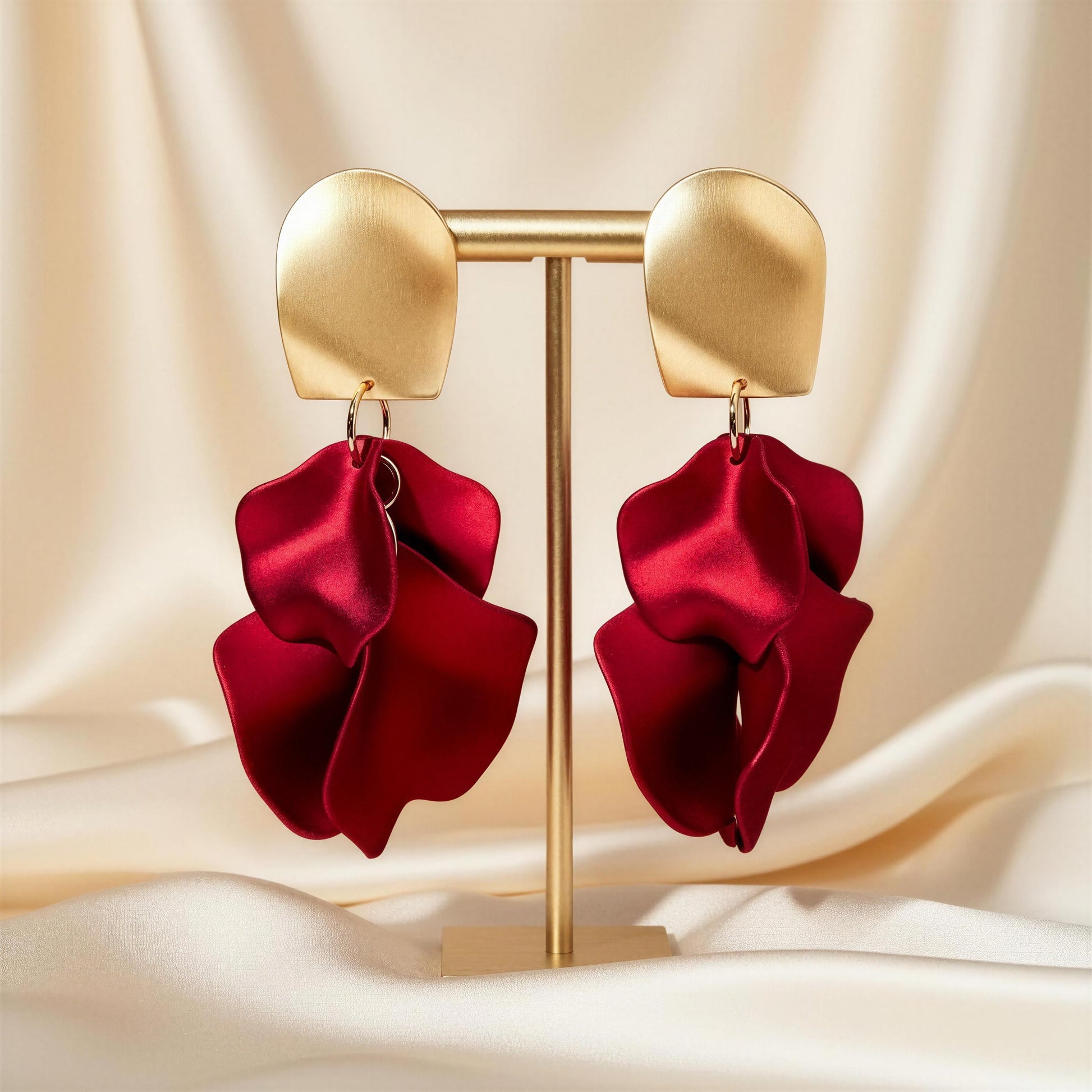 The Crimson Bloom Earrings with red satin bows on a beige fabric background