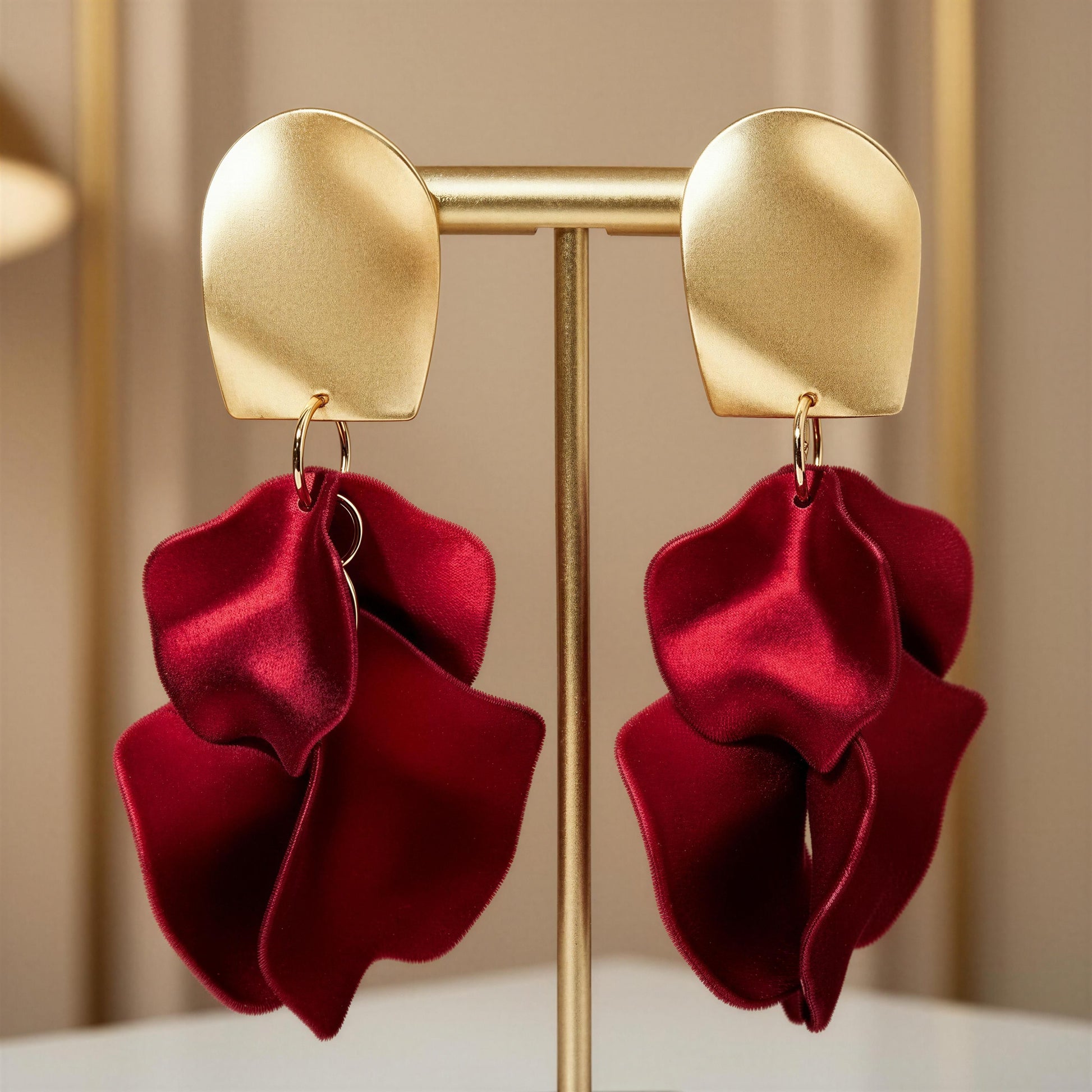 The Crimson Bloom Earrings with red floral drops on a gold stand against a beige background