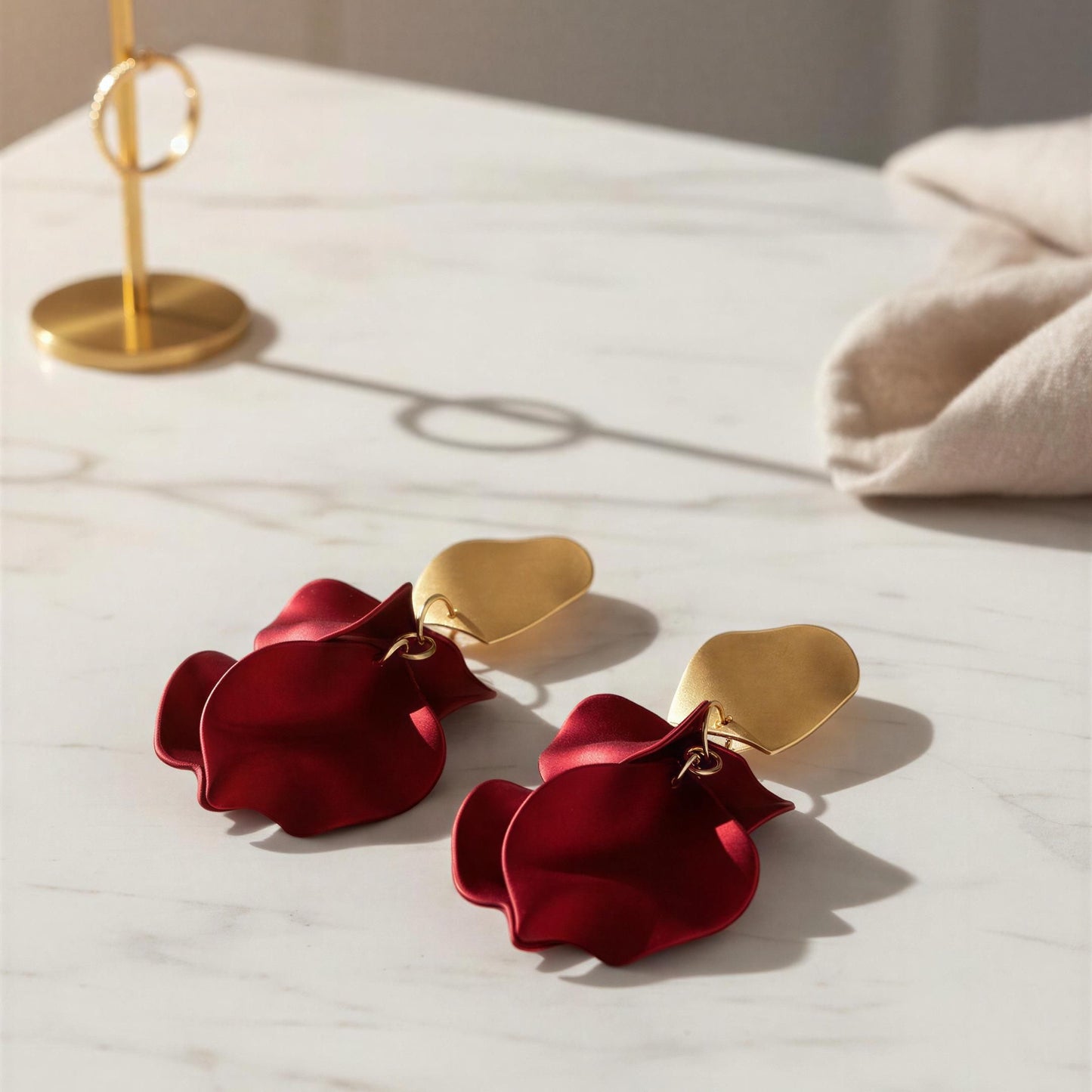 Red flower-shaped earrings with gold heart accents on a marble surface.