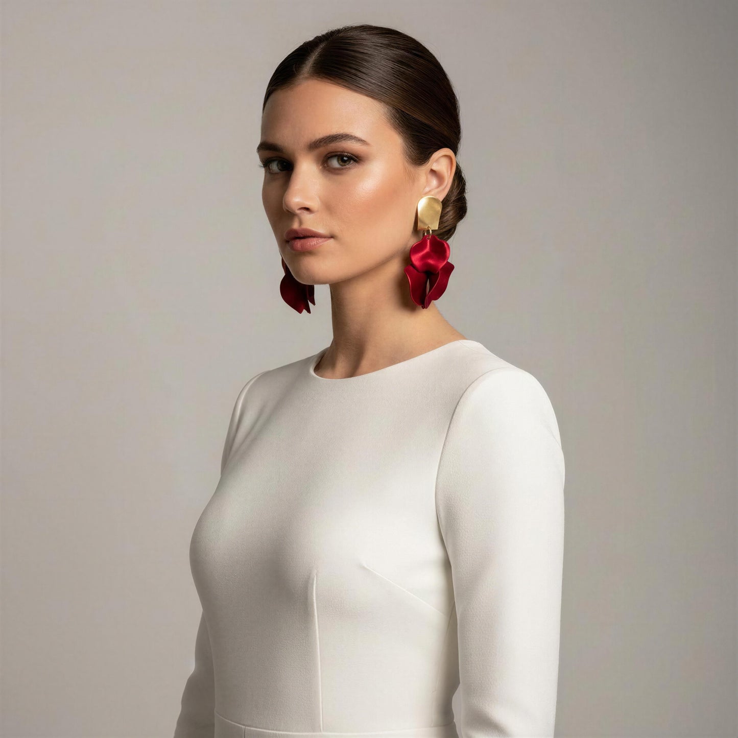 Woman wearing a white dress and the Crimson Bloom Earrings against a neutral background