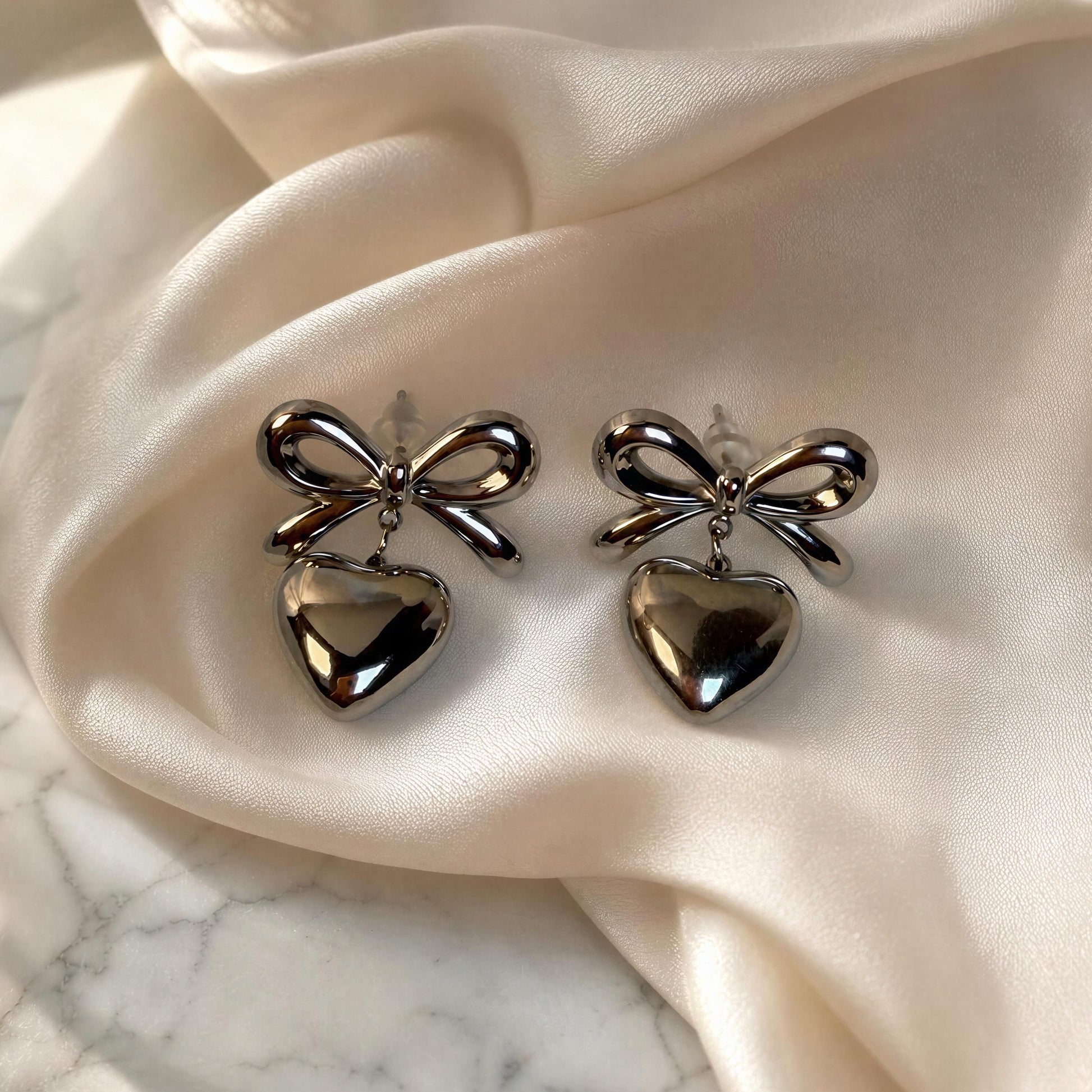 The Cupid's Knot Earrings - Silver against silk fabric on marble vanity table 