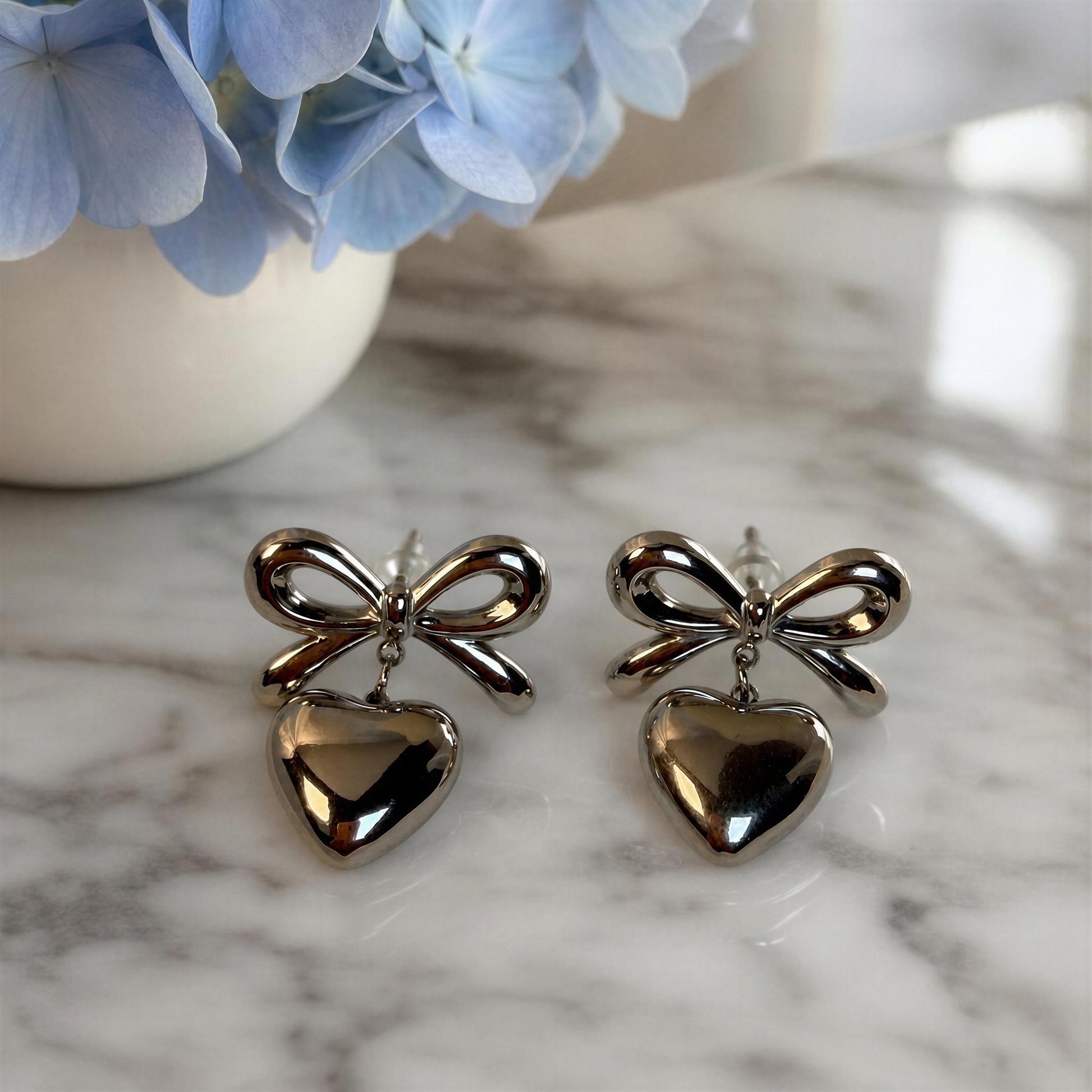 The Cupid's Knot Earrings - Silver on marble table beside a vase with light blue hydrangeas