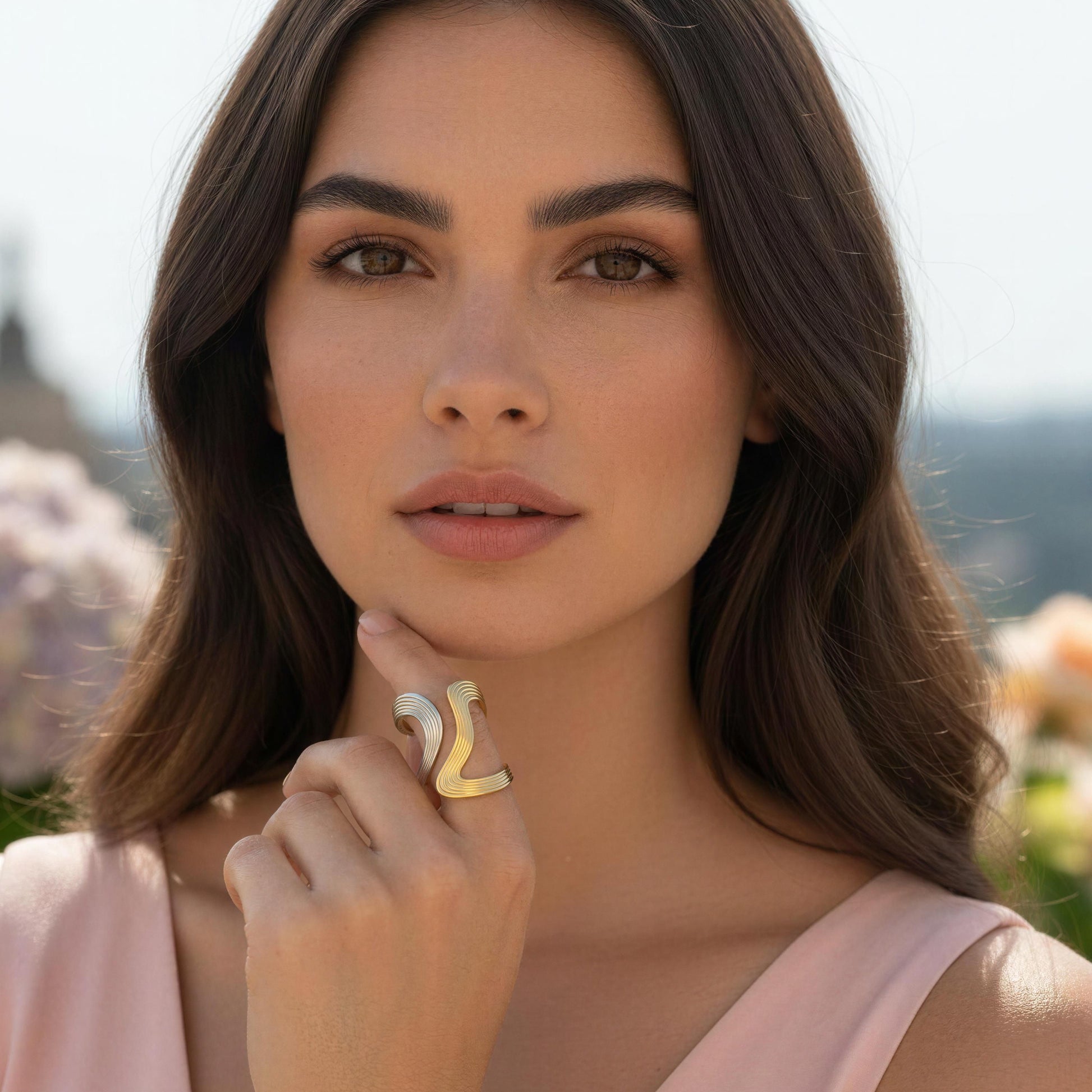 Woman wearing the Dawn & Dusk Wave Ring with a blurred floral background