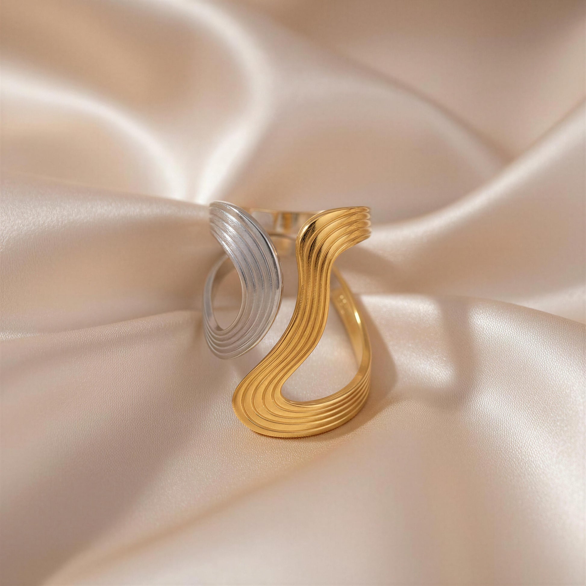 Dawn & Dusk Wave Ring; a gold and silver ring on a soft pink satin background