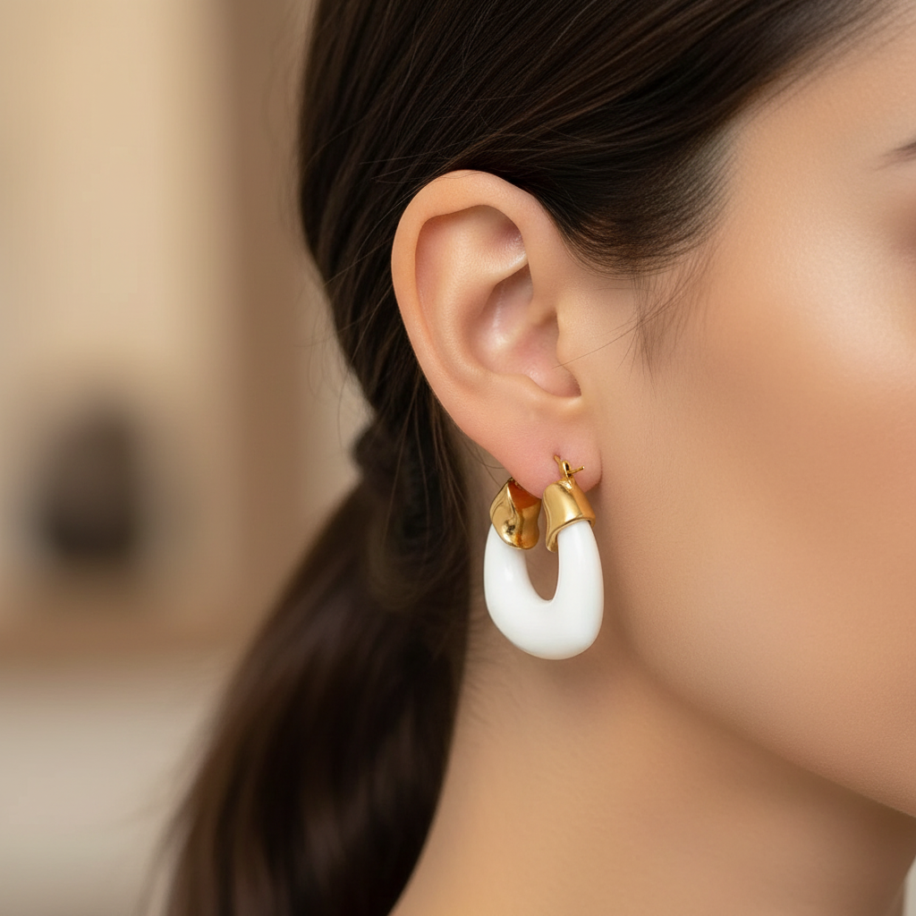Close-up of a person wearing the Deco White Hoops - Chica Chica Jewelry  gold and white hoop earrings with blurred background