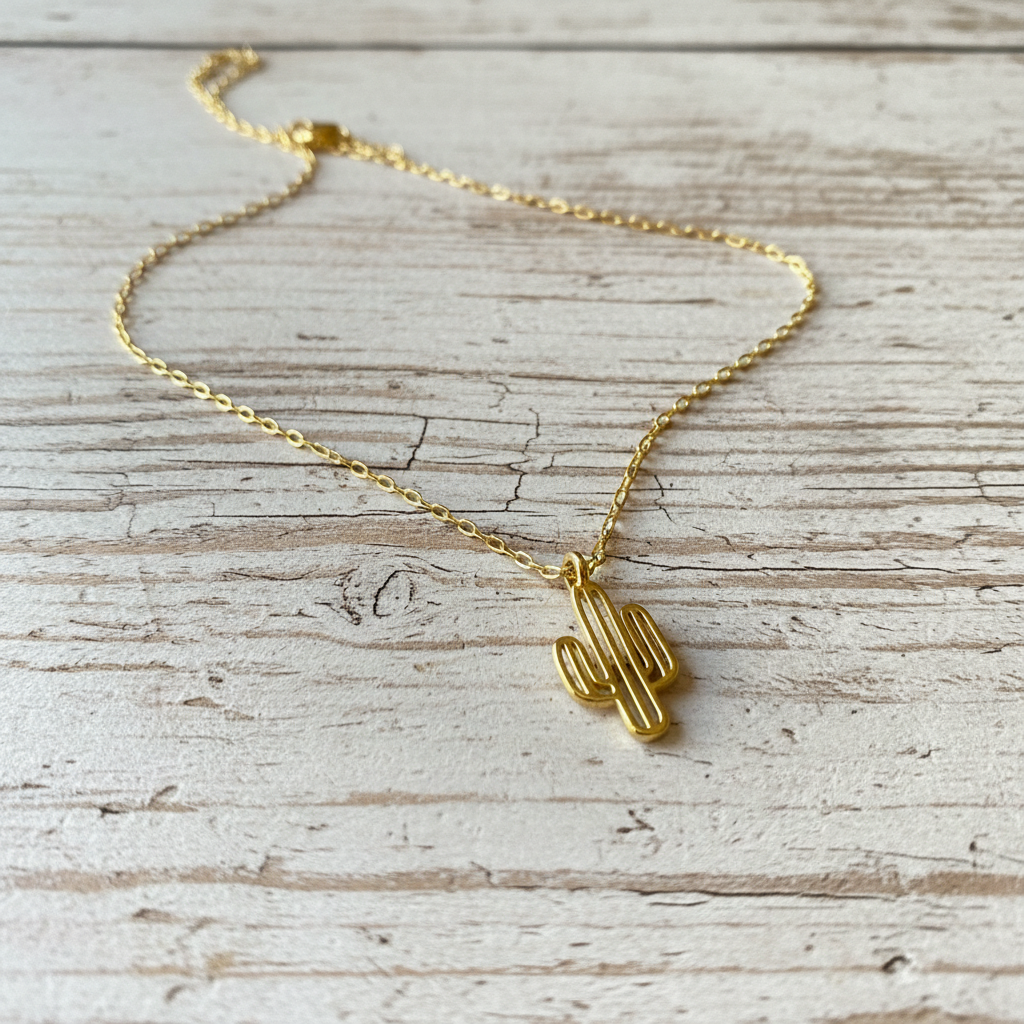 Gold cactus-shaped pendant necklace on a light wooden surface from Chica Chica Jewelry