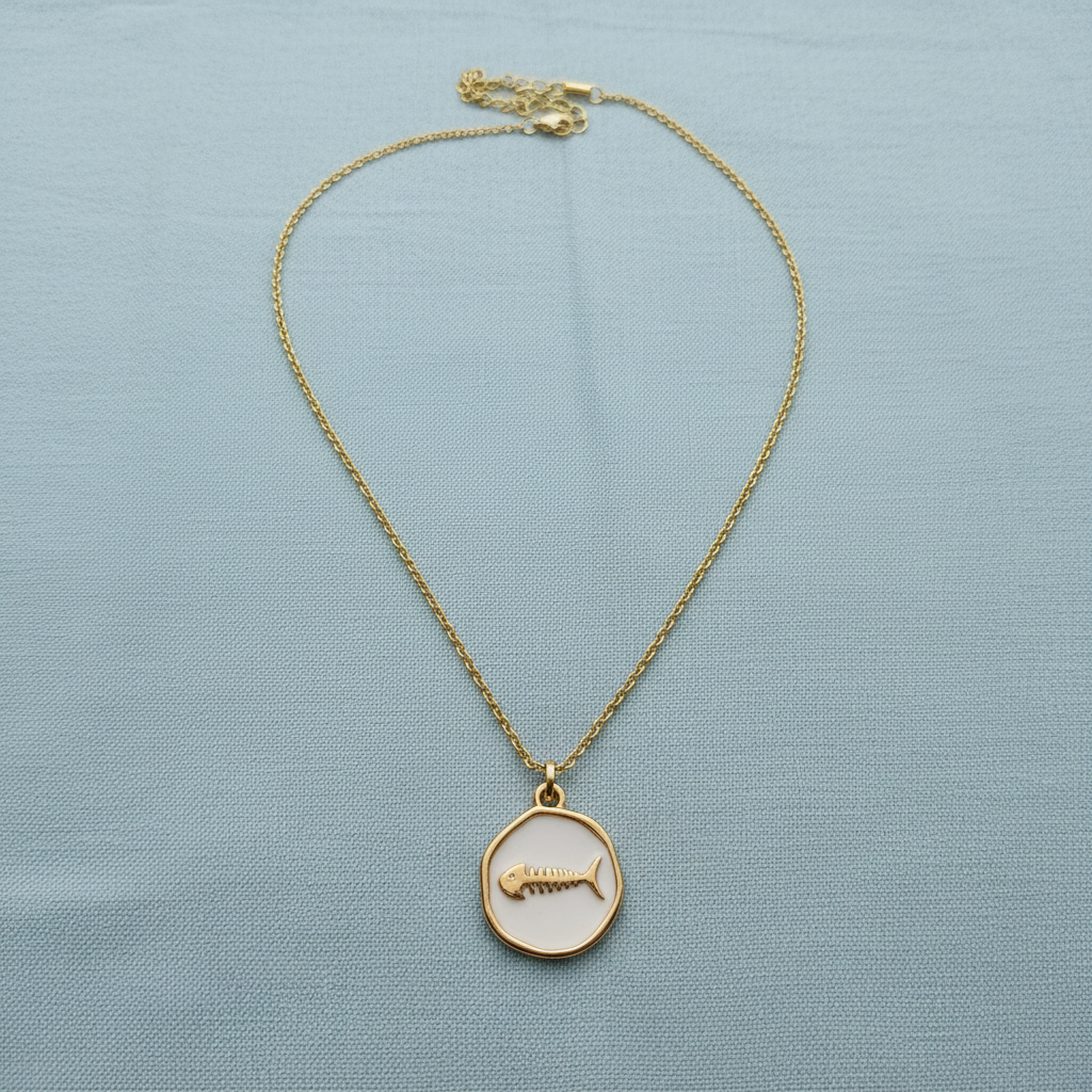 Driftmark Fish Necklace on a light blue fabric background